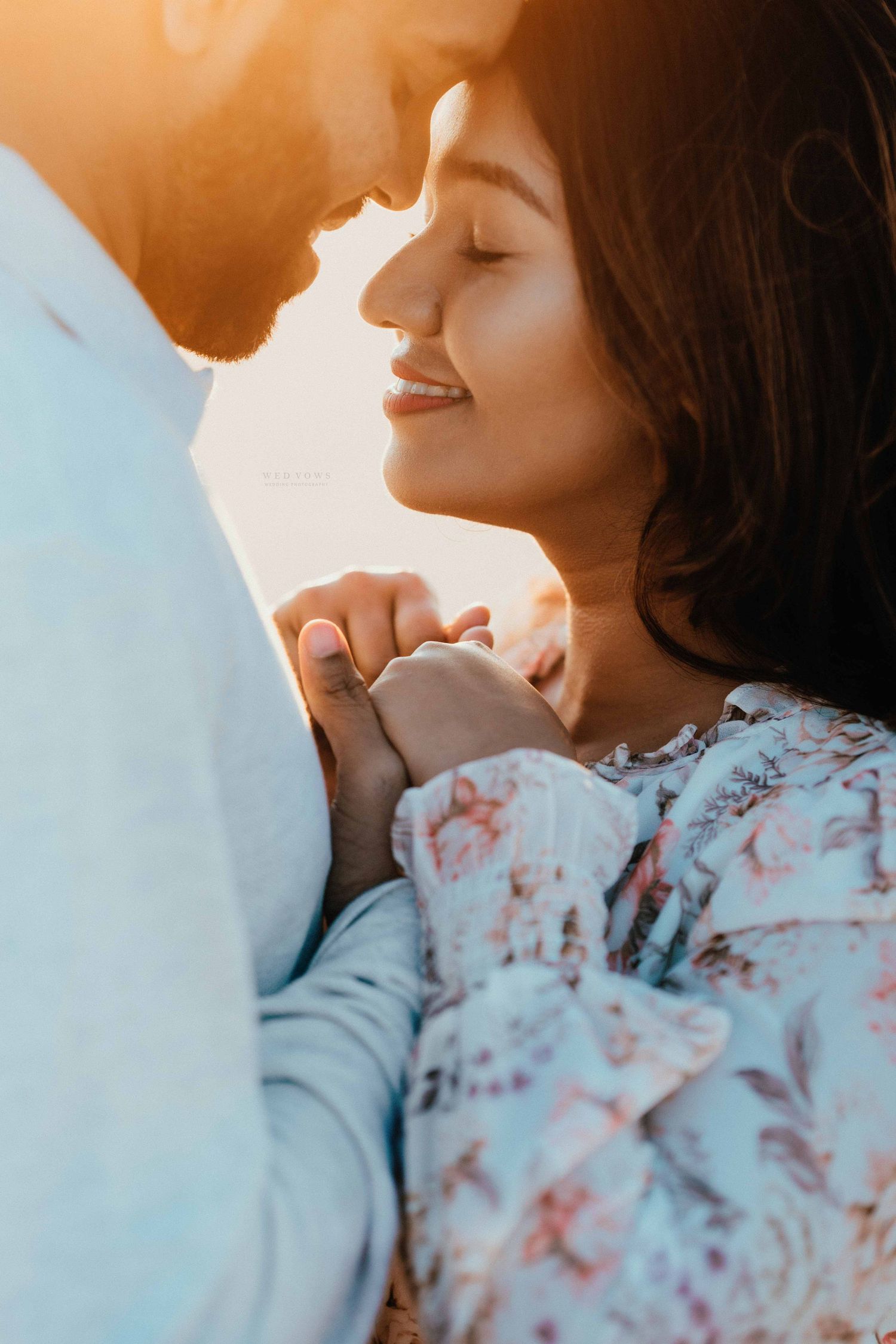Romantic couple nearly kissing at golden sunset, woman smiling with eyes closed while holding hands tenderly.