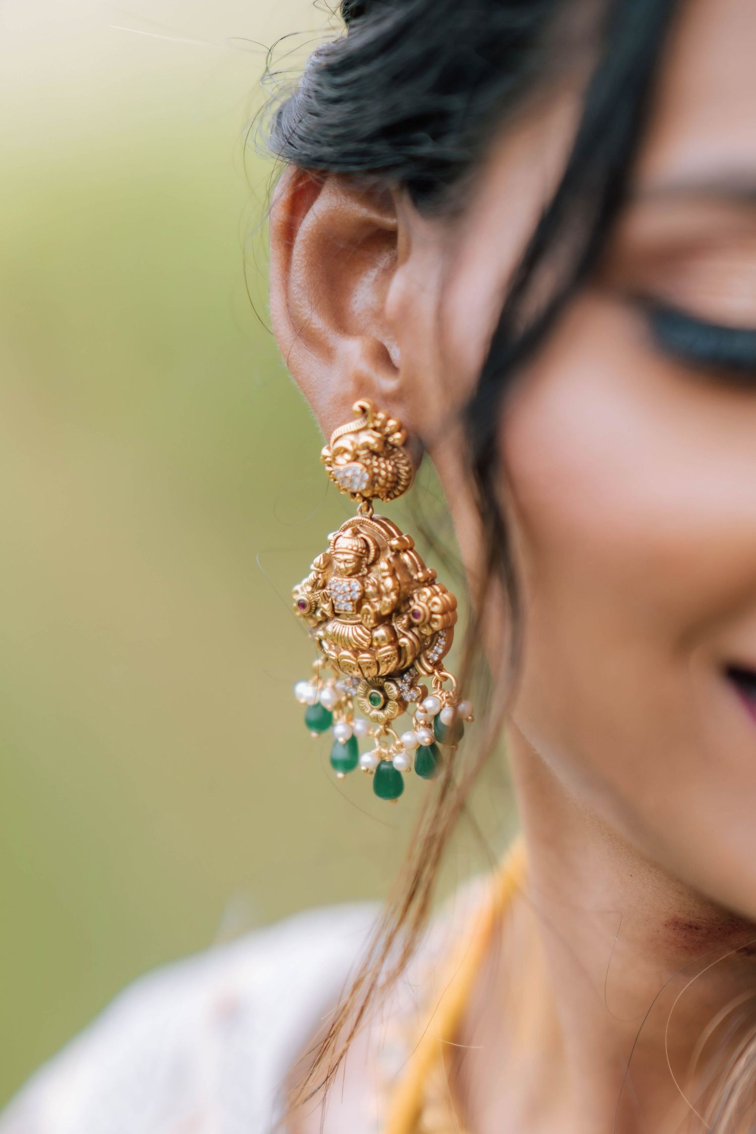 Close-up of Indian bride wearing intricate gold temple jhumka earrings with emerald and pearl drops.