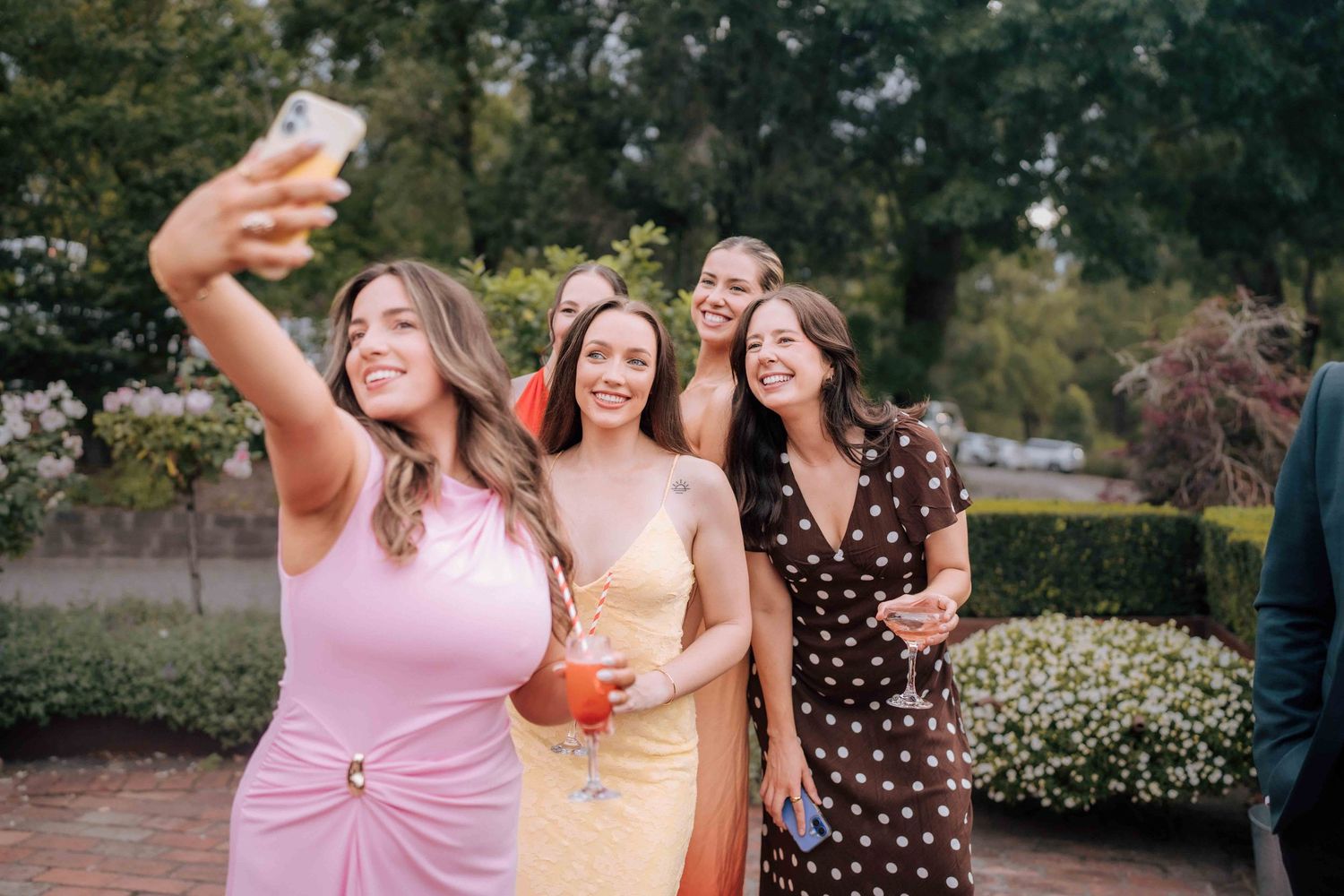 Group of women in formal dresses taking a selfie at an outdoor wedding celebration.