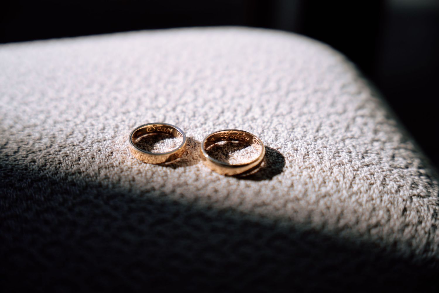 Two gold wedding rings resting on a textured white surface in soft natural light.