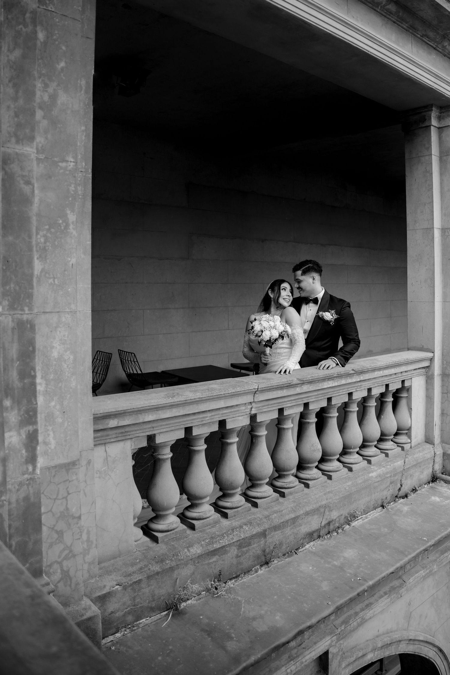 Black and white photo of bride and groom sharing an intimate moment on a stone balcony.