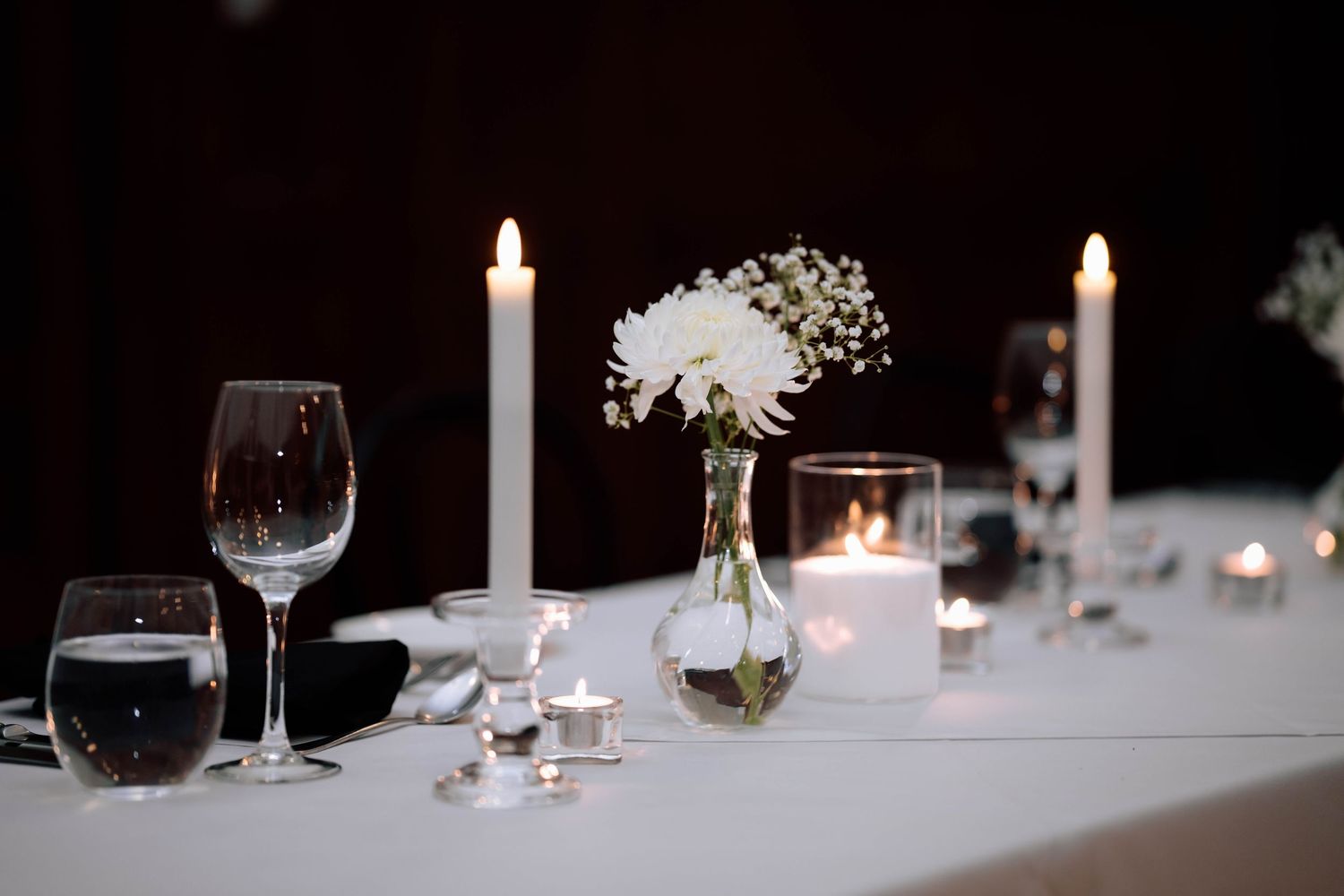 Elegant wedding reception table with white candles, crystal glasses, and white floral centerpiece.