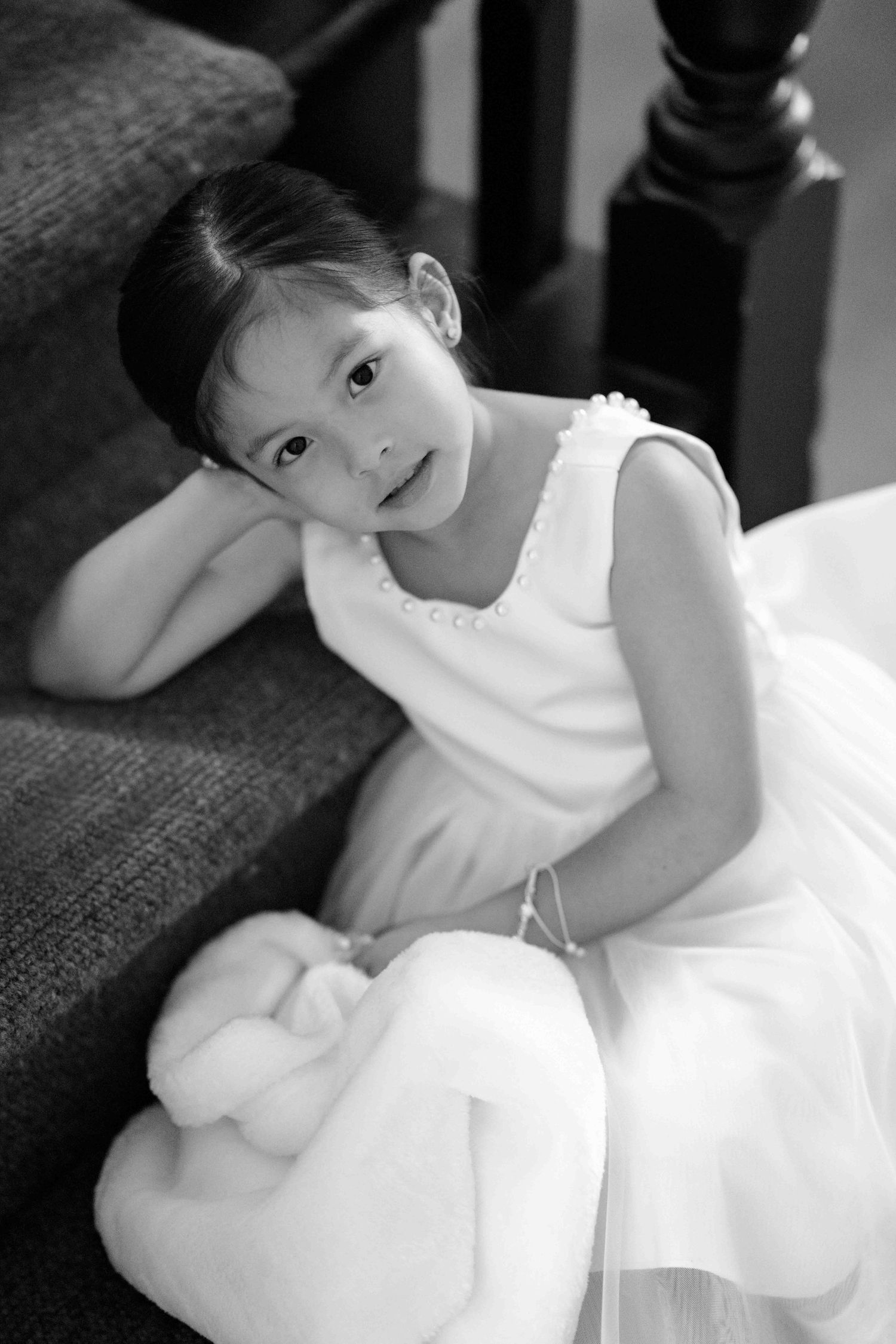 Adorable flower girl in white dress sitting on staircase at wedding.
