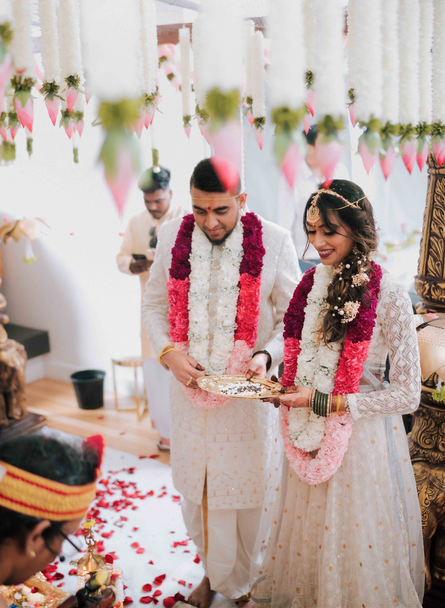 Hindu bride and groom performing wedding rituals together wearing white outfits and floral garlands.