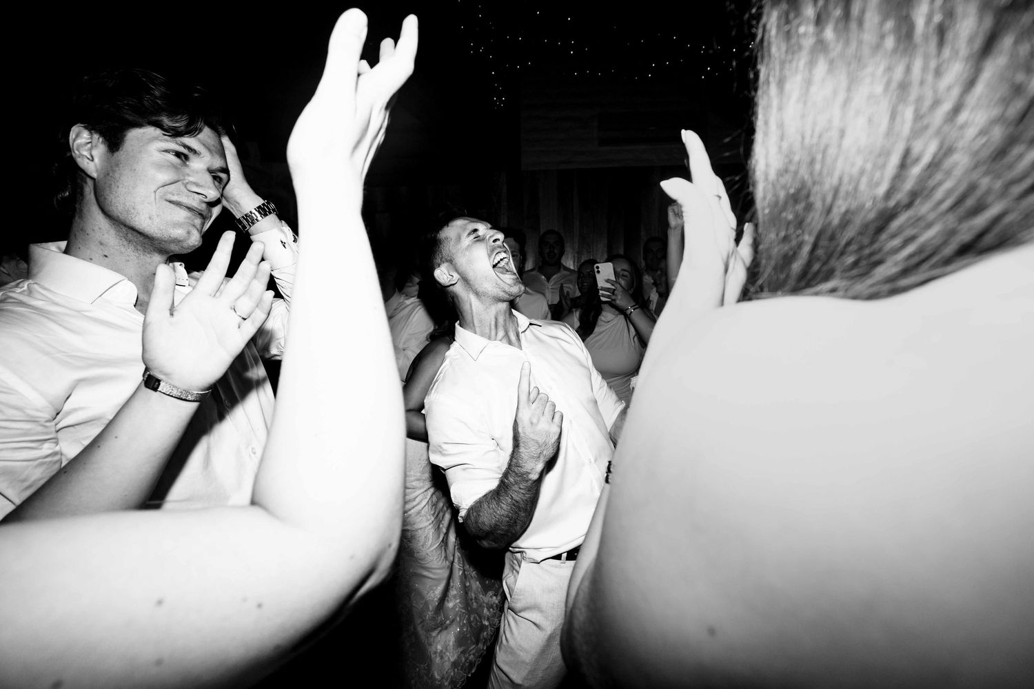 Black and white photo of guests dancing energetically at a wedding reception party.