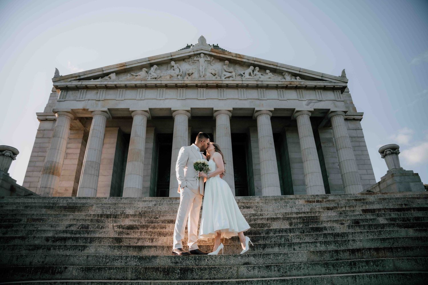 Wedding couple embracing on steps before a grand neoclassical building with tall columns.