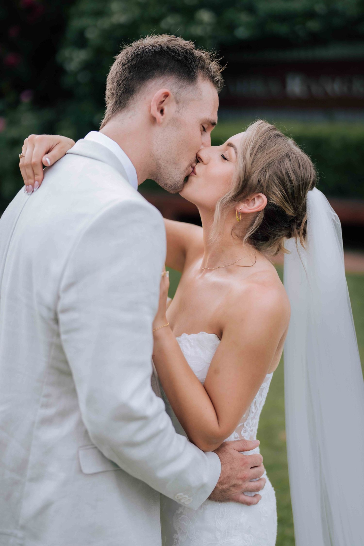Bride and groom sharing a romantic kiss outdoors on their wedding day, groom in white suit.
