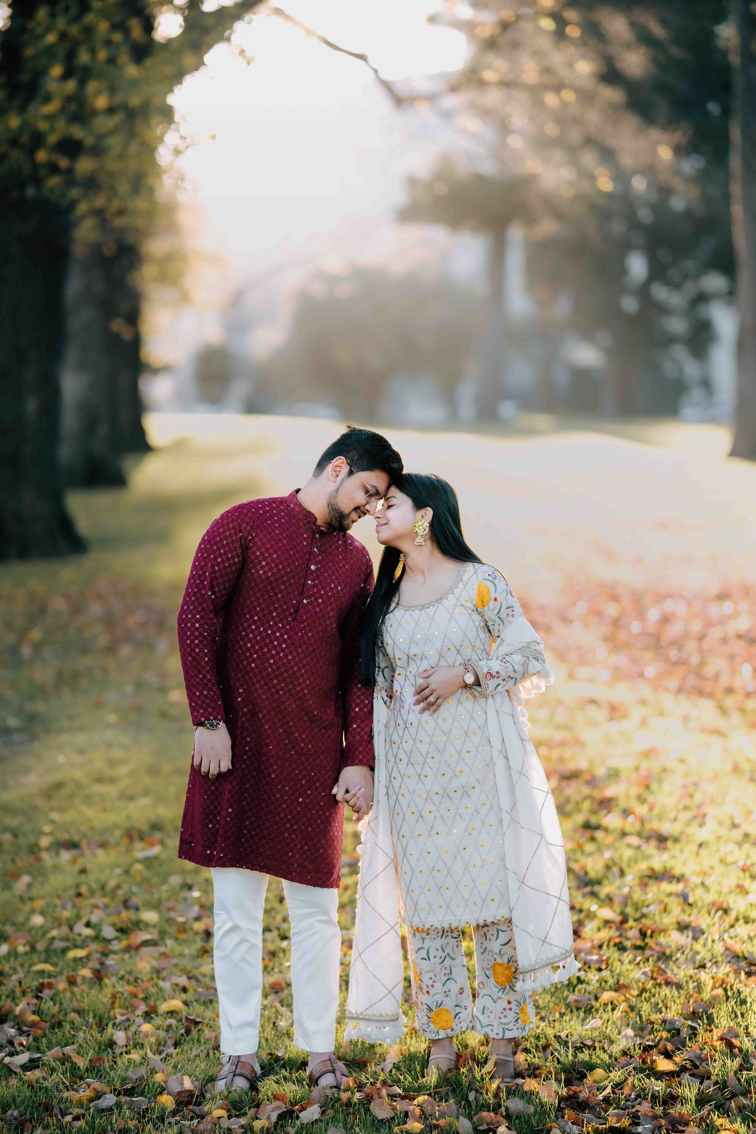South Asian couple sharing a tender kiss in a golden autumn park setting.