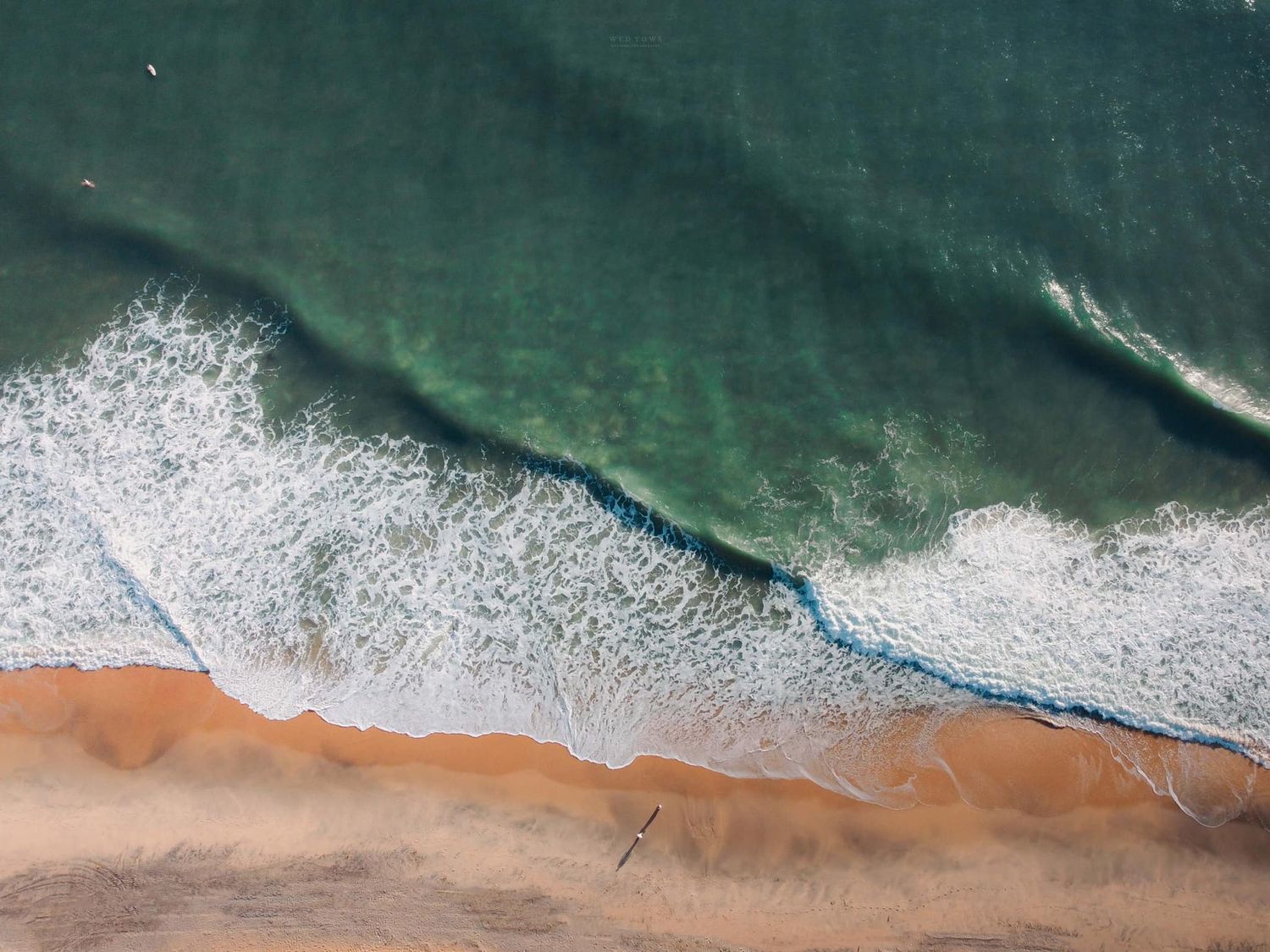 Aerial view of turquoise ocean waves meeting a sandy beach shoreline.