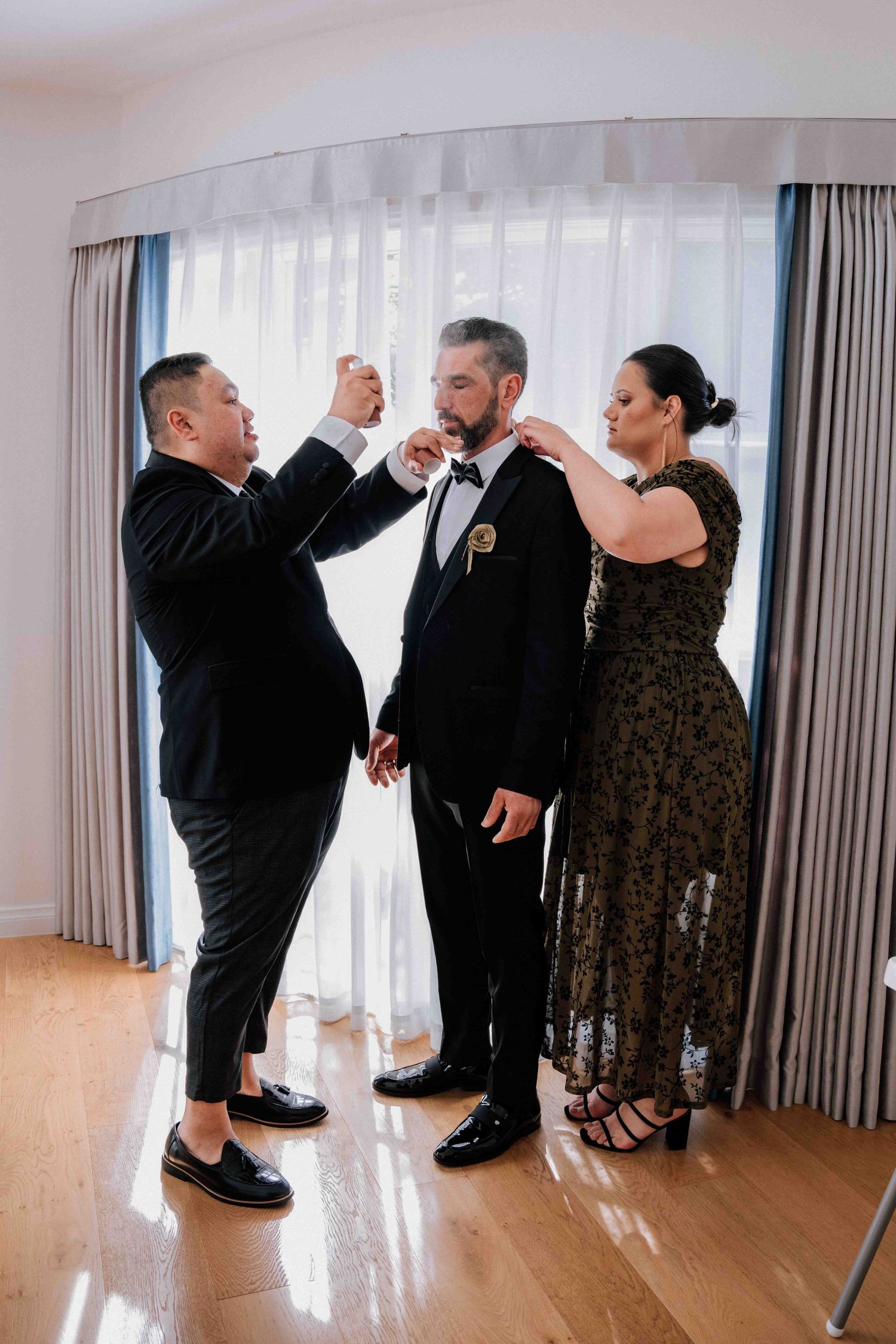 Groom being helped by two attendants adjusting his bow tie and boutonniere before the wedding ceremony.