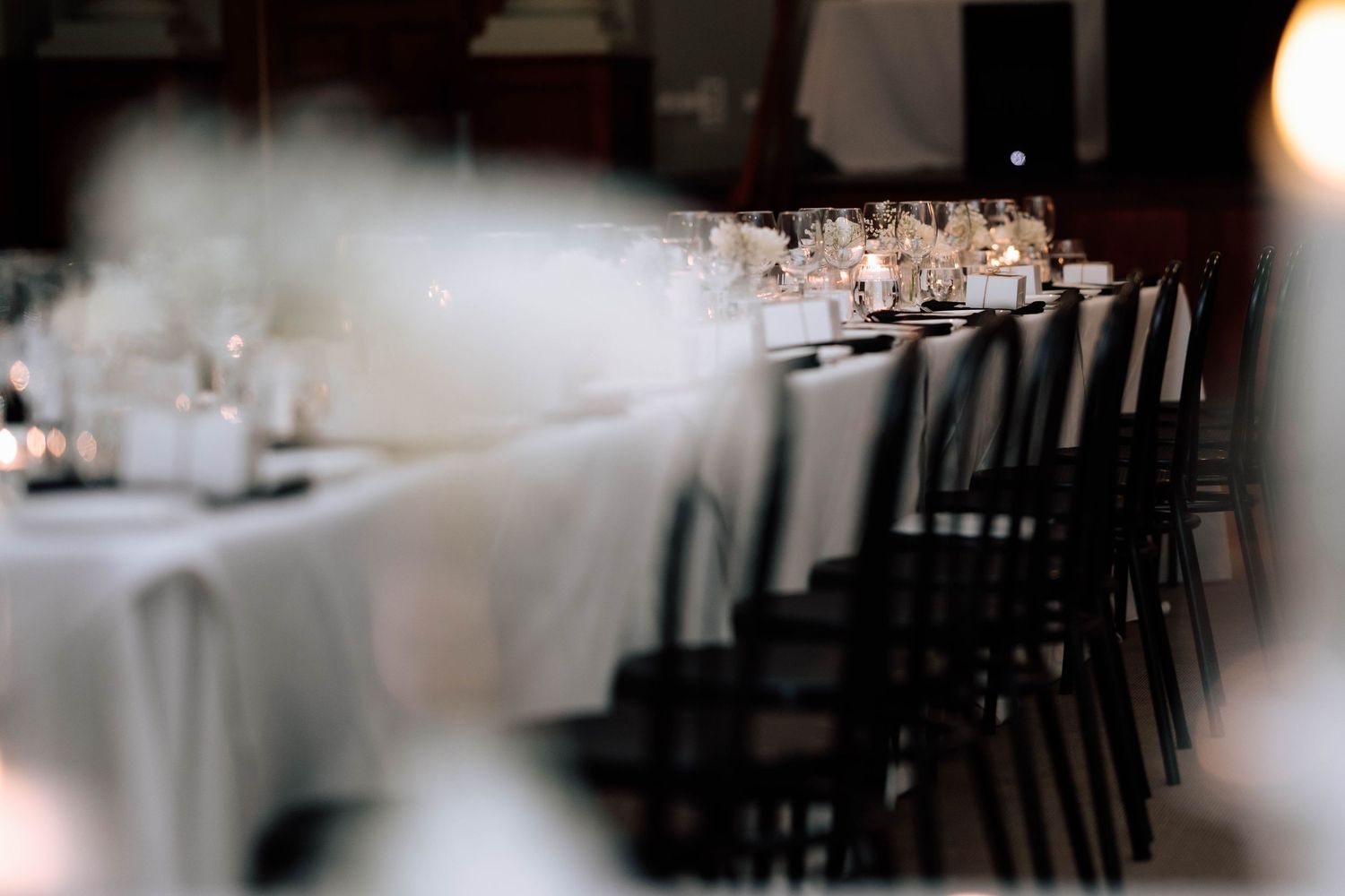 Elegantly set long reception table with white linens, candles, and glassware in a dimly lit venue.