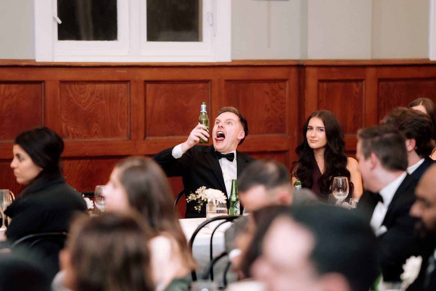Wedding guest enthusiastically toasts with a bottle during the reception dinner celebration.