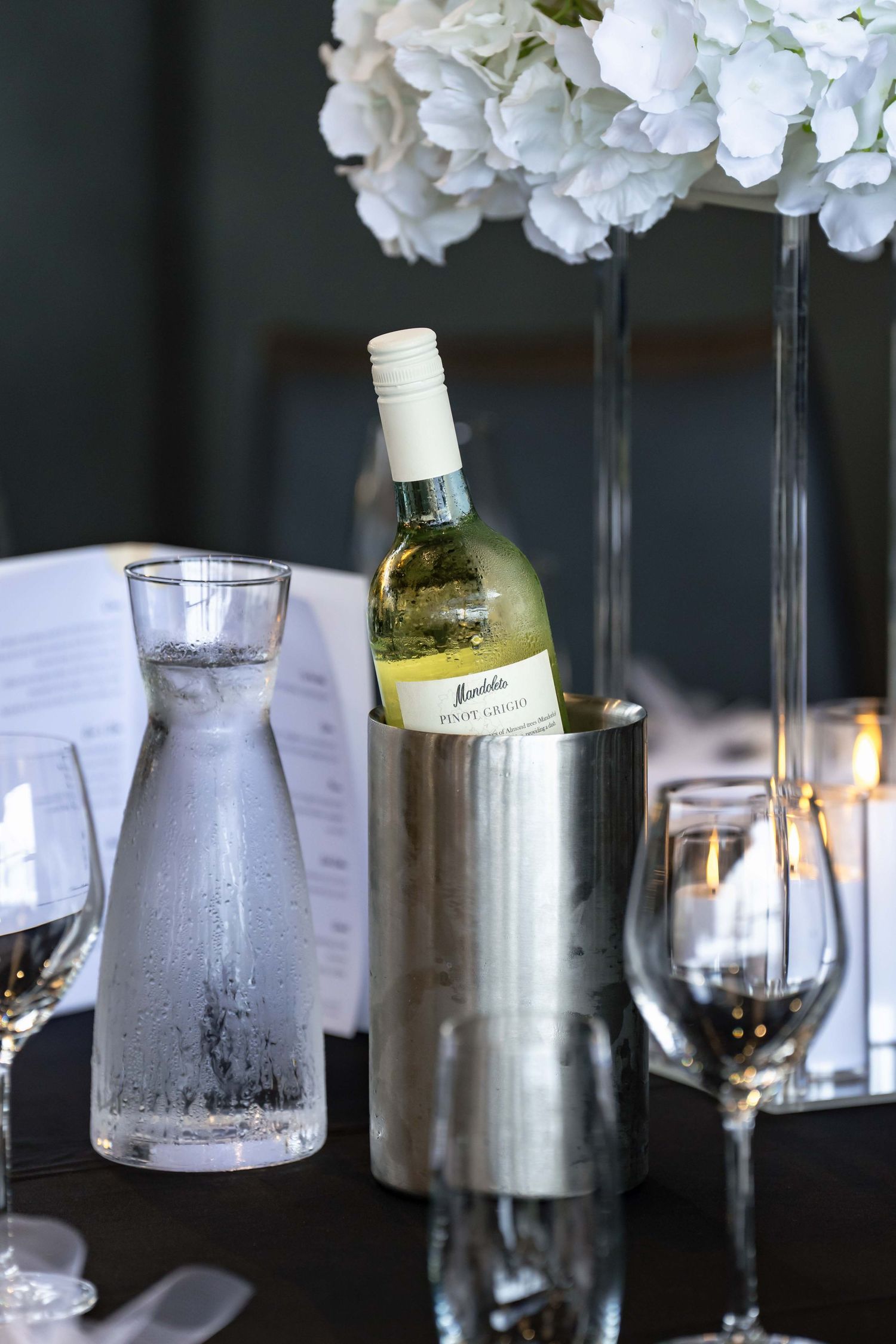 A bottle of Pinot Grigio in a silver wine cooler on an elegantly set wedding reception table.