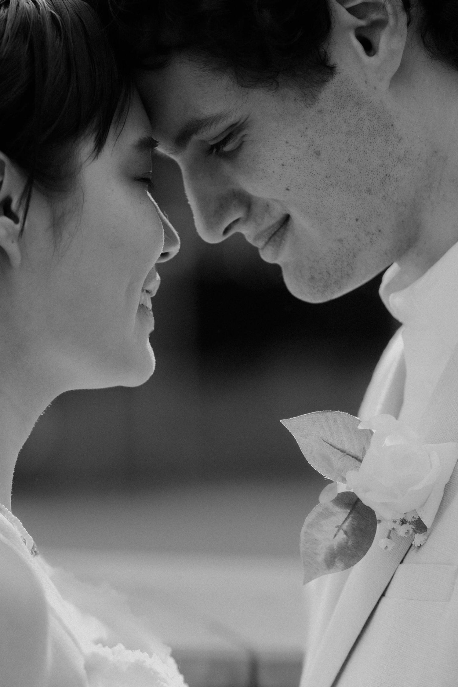 Romantic black and white close-up of bride and groom facing each other and smiling tenderly.