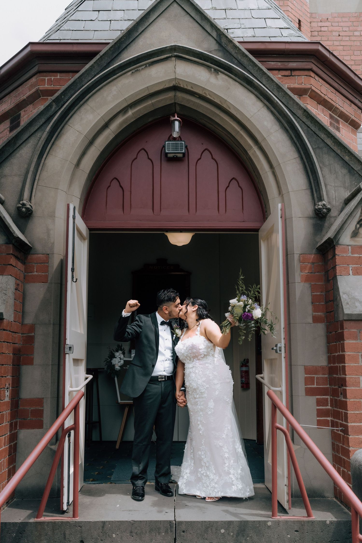 Newlyweds sharing a kiss at the entrance of a brick church after wedding ceremony.