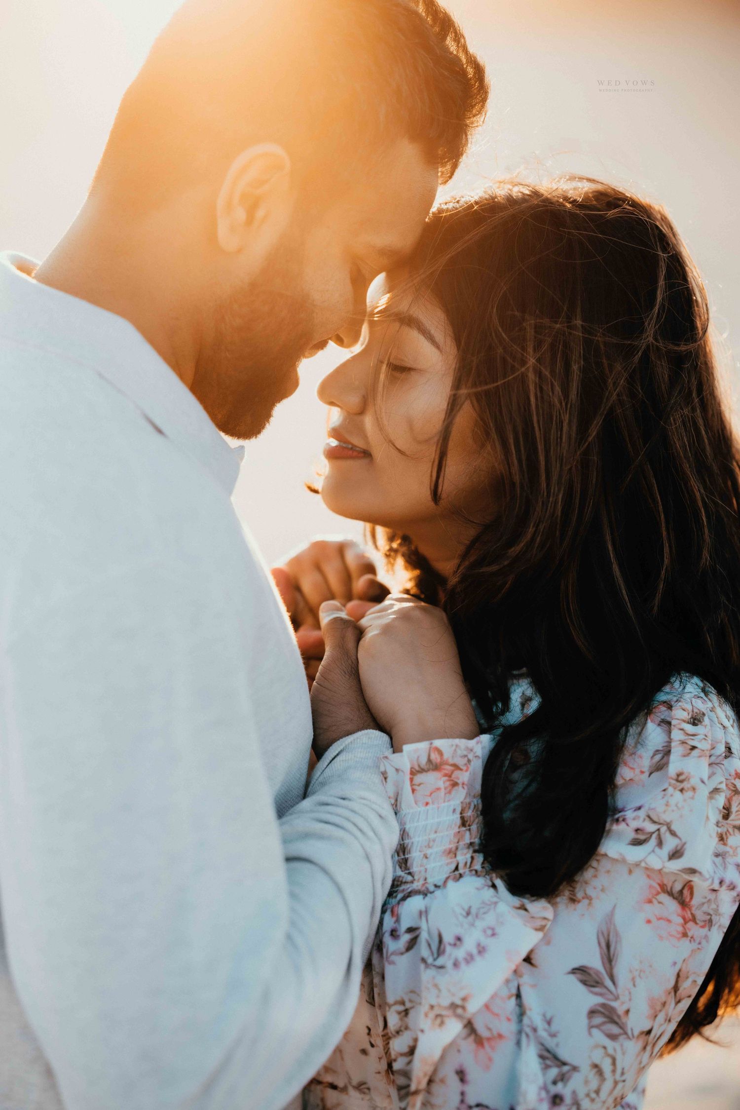 Romantic couple touching foreheads in warm sunset backlight, holding hands tenderly outdoors.