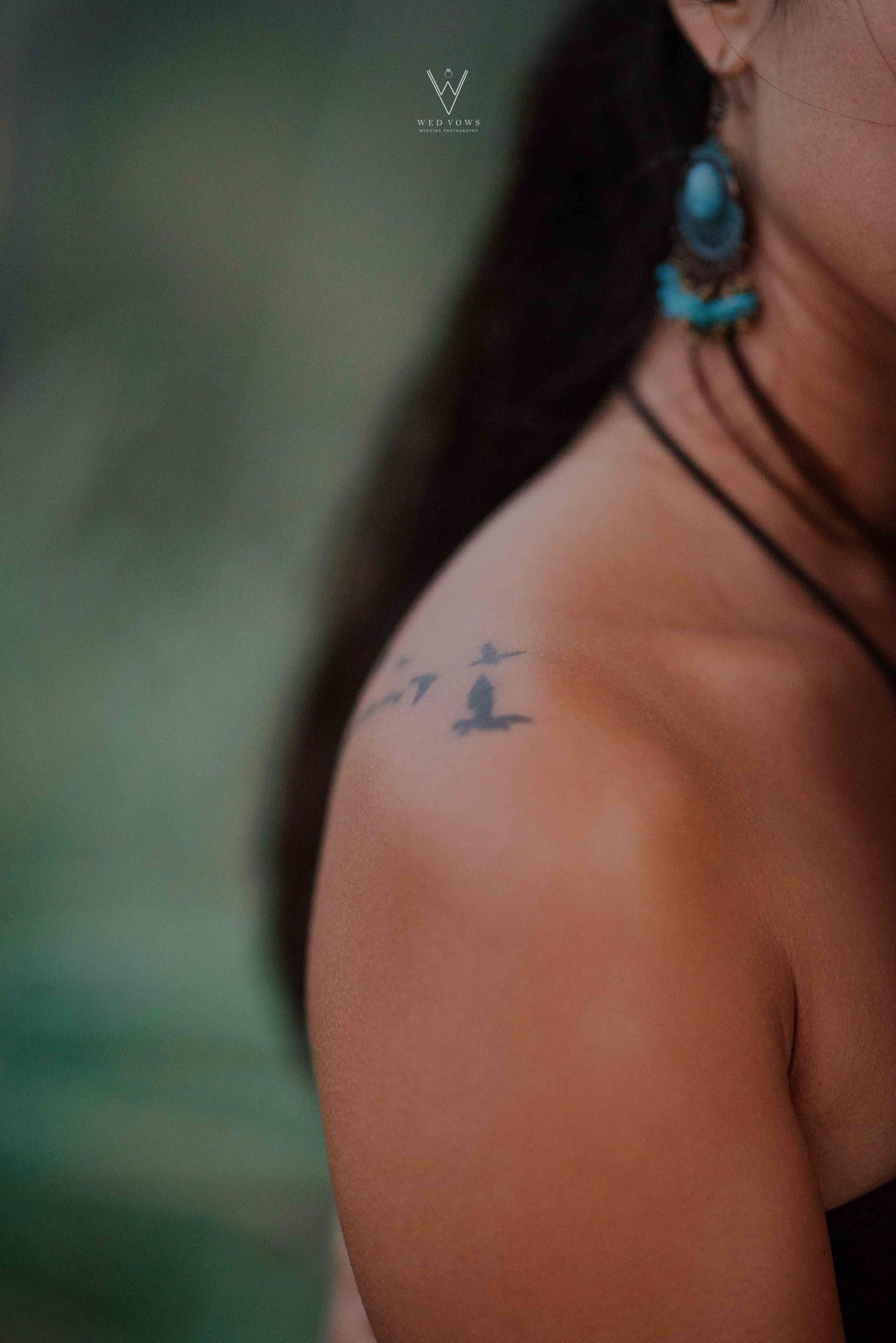 Close-up of woman's shoulder tattoo of flying birds with turquoise earring detail.
