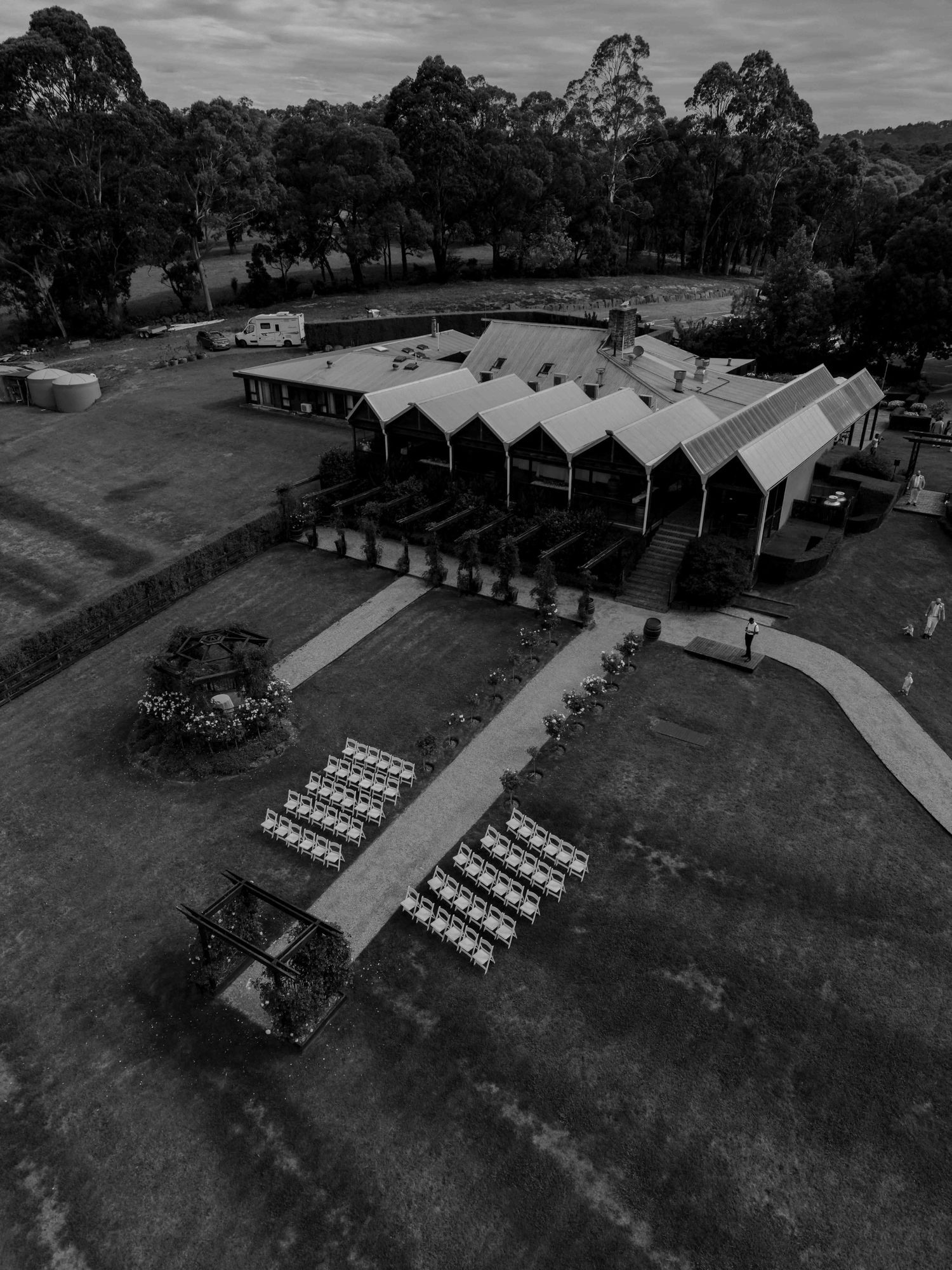 Aerial black and white view of outdoor wedding venue with rows of white chairs on manicured grounds.