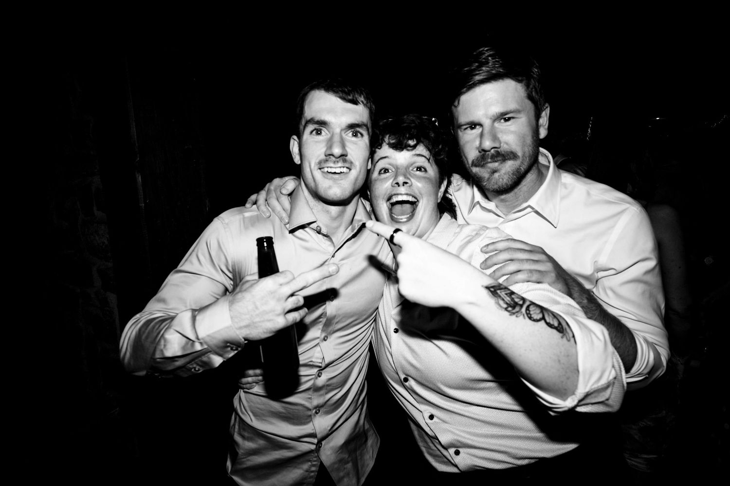 Three wedding guests pose playfully in black and white photo at reception.