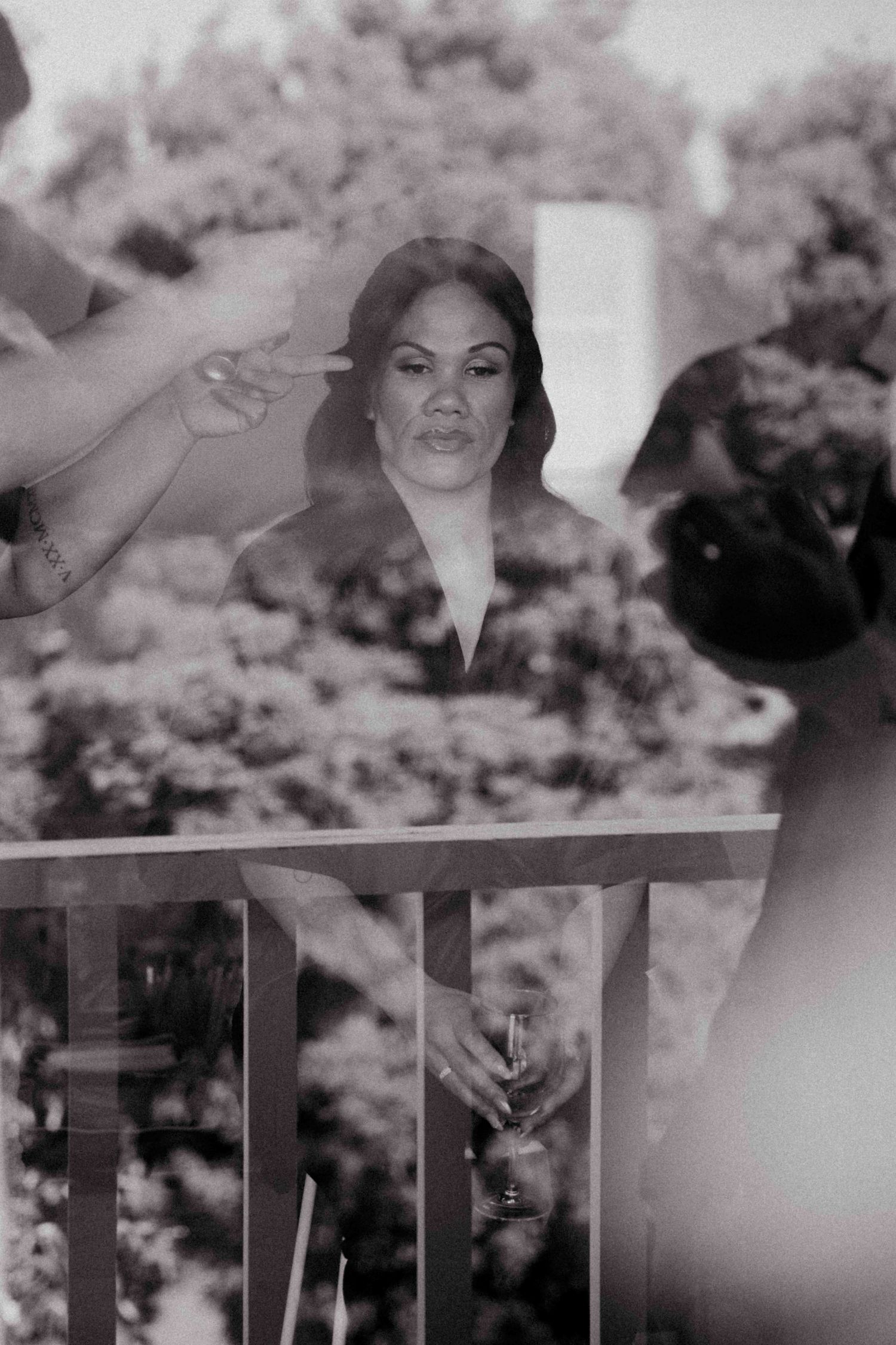 Black and white photo of a bridesmaid holding a champagne glass on a balcony surrounded by lush greenery.