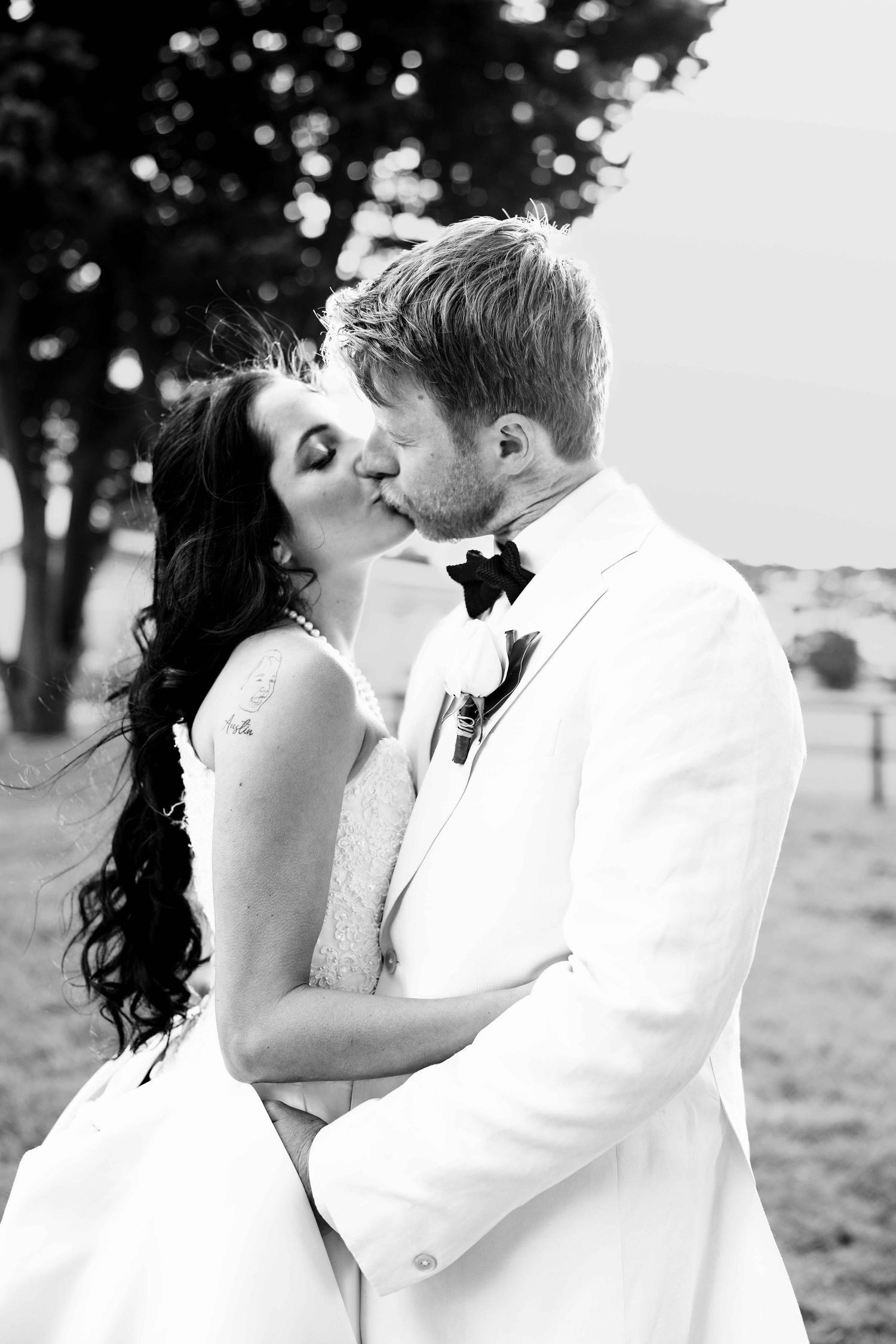 Black and white photo of bride and groom sharing a kiss outdoors on their wedding day.