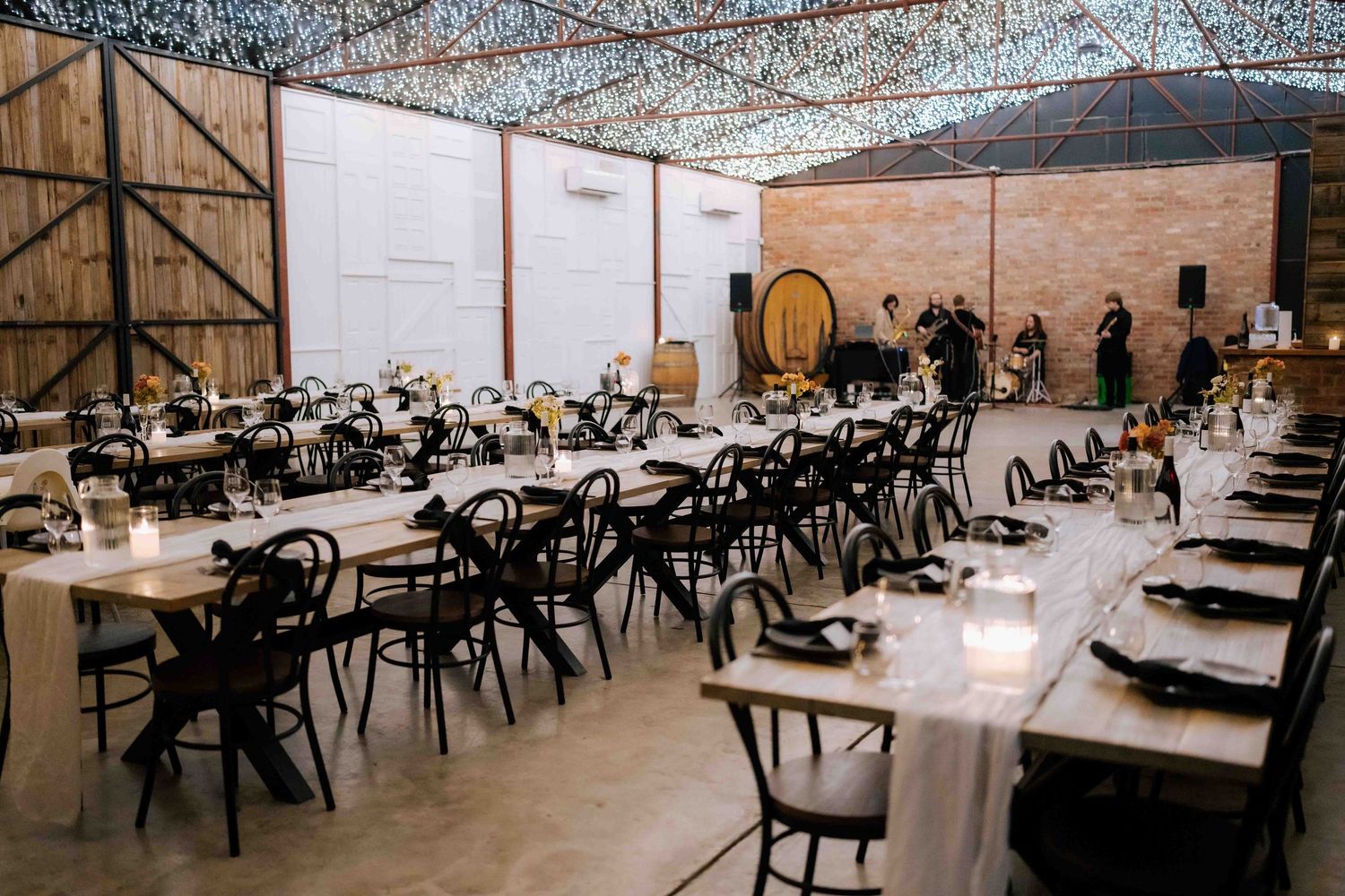 Elegant wedding reception setup with long tables, black chairs, candles, and fairy light ceiling.