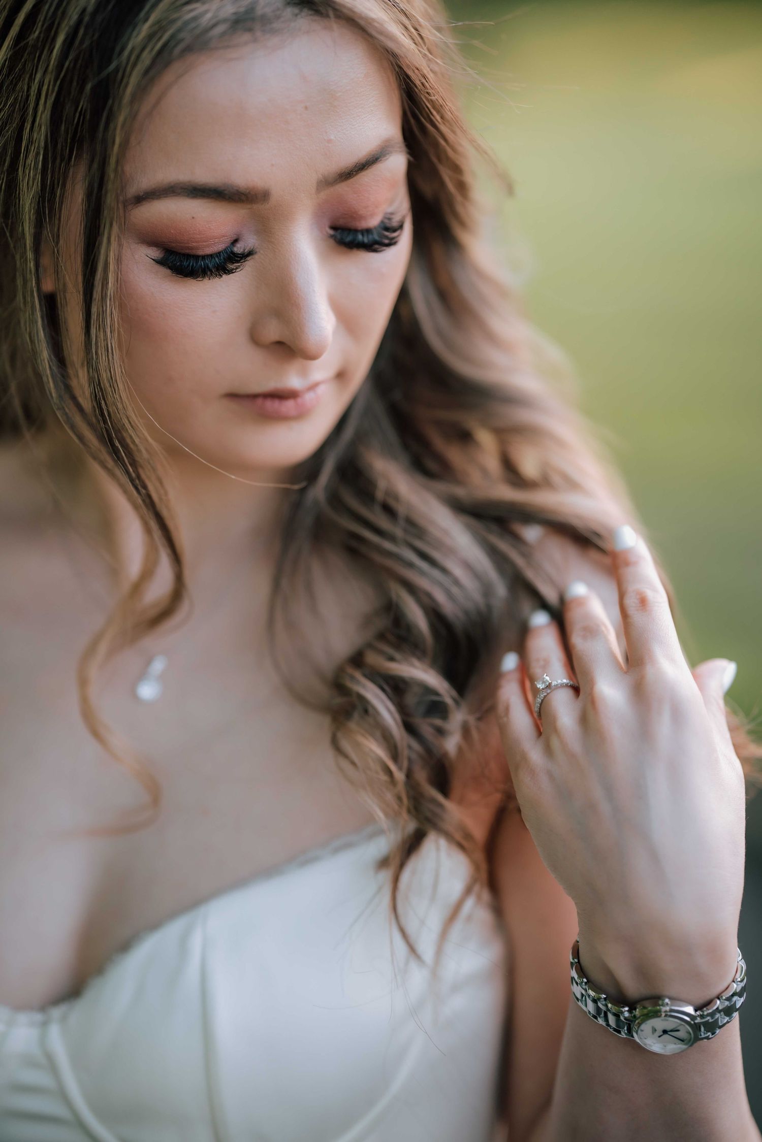 Close-up of a bride with elegant makeup, wavy hair, and a diamond engagement ring on her finger.