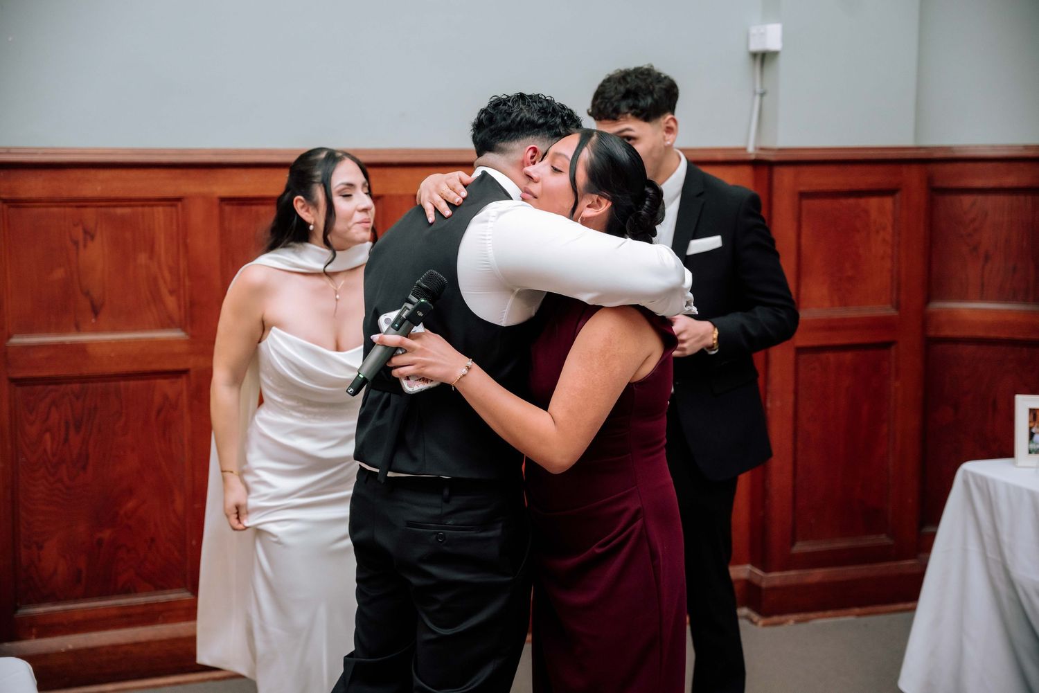 Emotional wedding guests embrace the groom in a heartfelt group hug during the reception celebration.