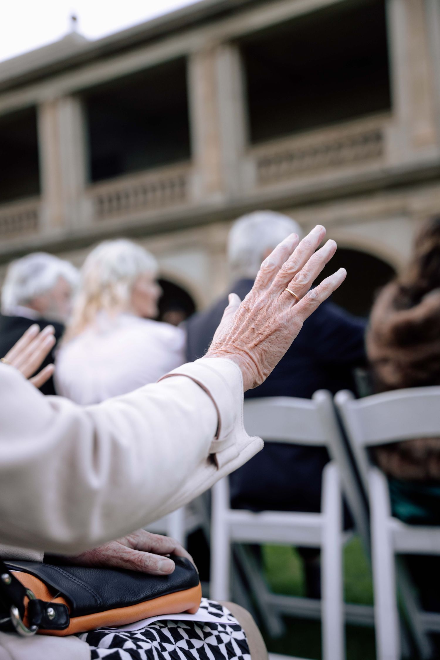 Elderly woman raises her hand in worship at an outdoor wedding ceremony.