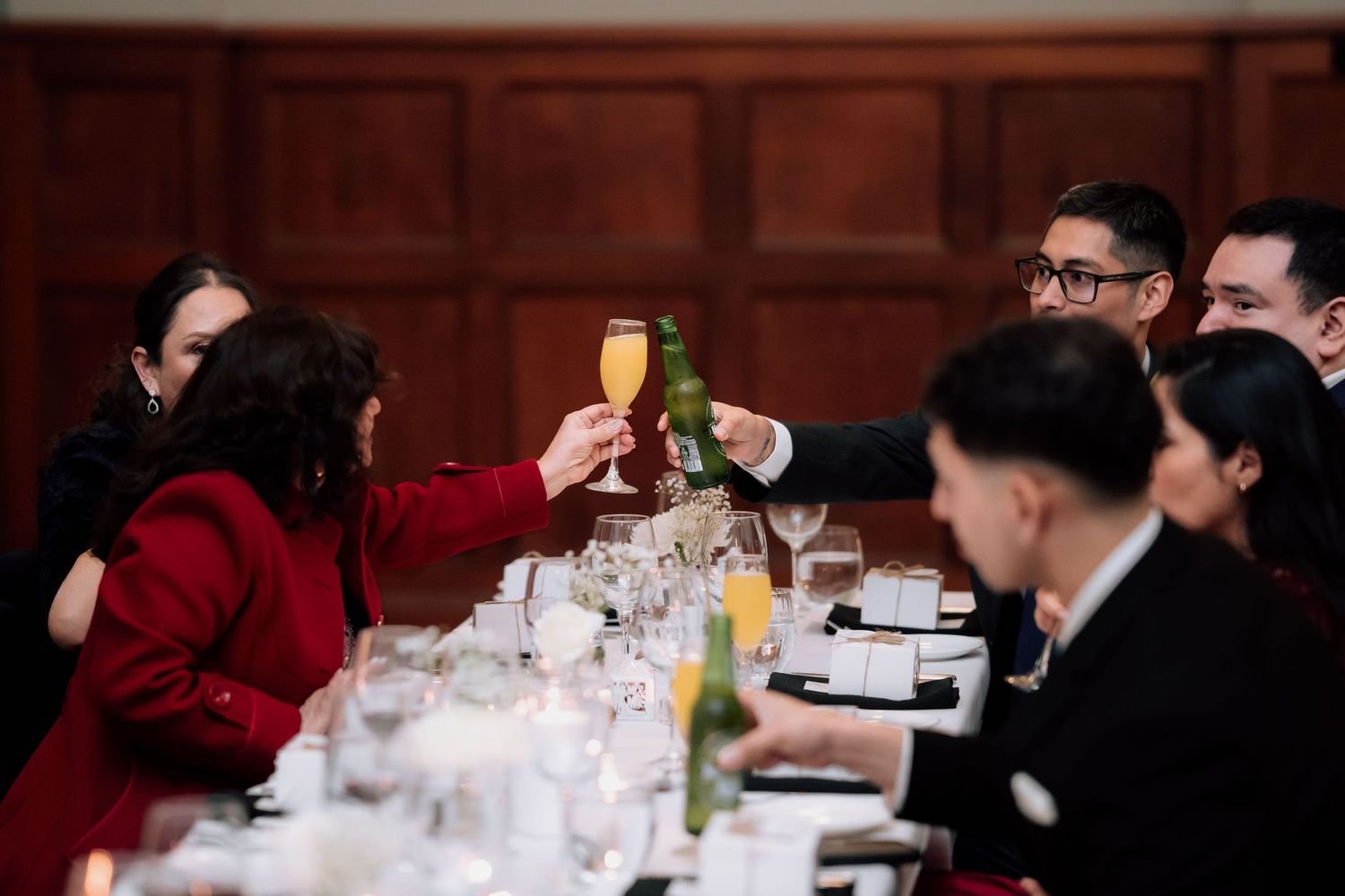 Wedding guests raise champagne glasses in a toast at a candlelit reception dinner table.
