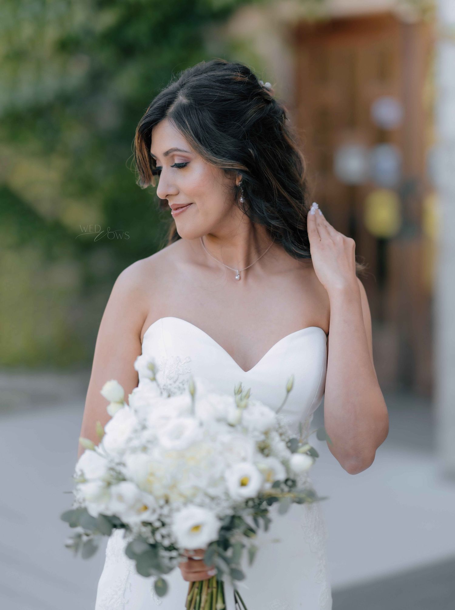 Elegant bride in strapless sweetheart gown holding white floral bouquet, looking down gracefully.