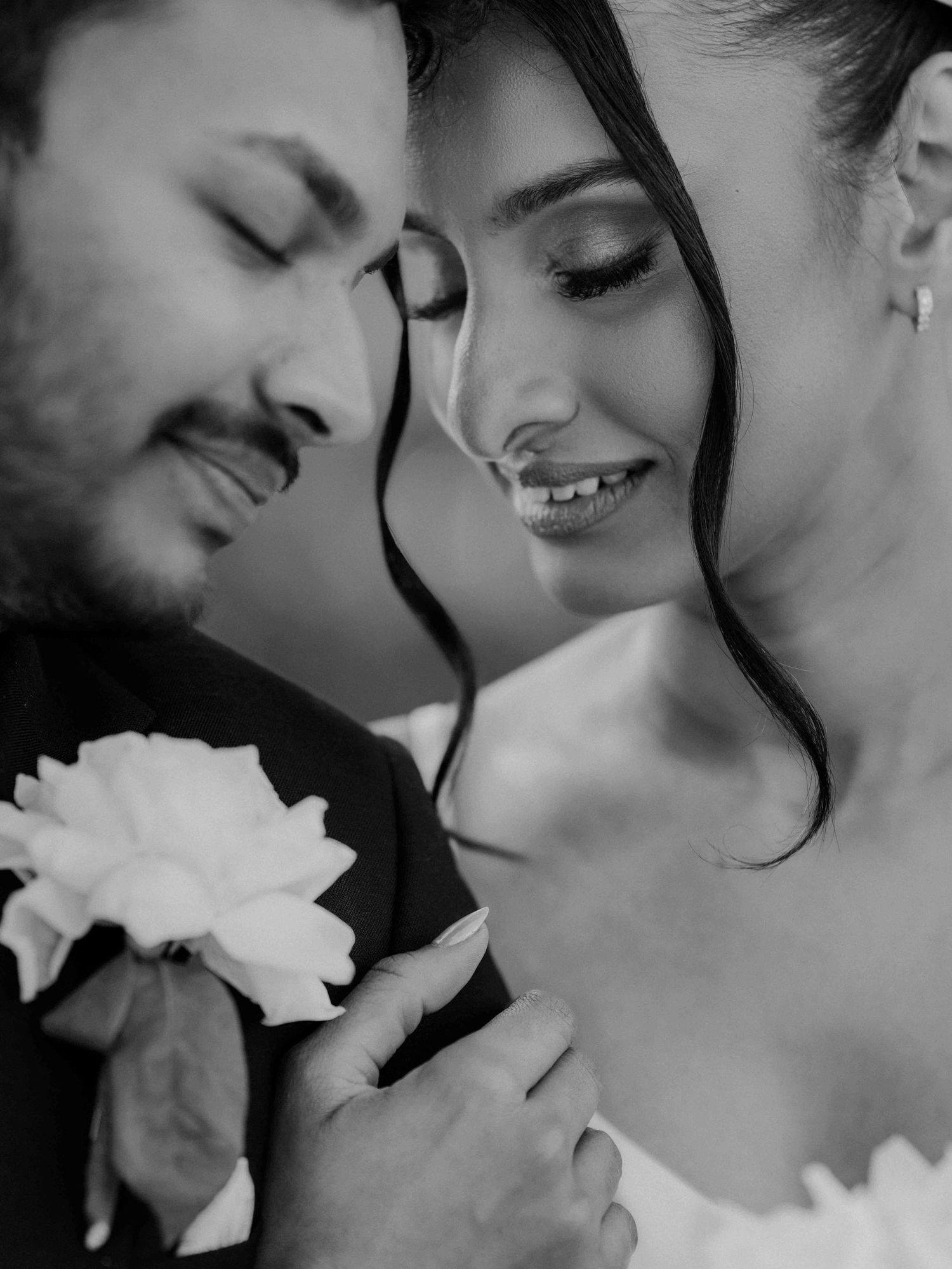 Black and white close-up of smiling bride and groom with boutonniere at their wedding.