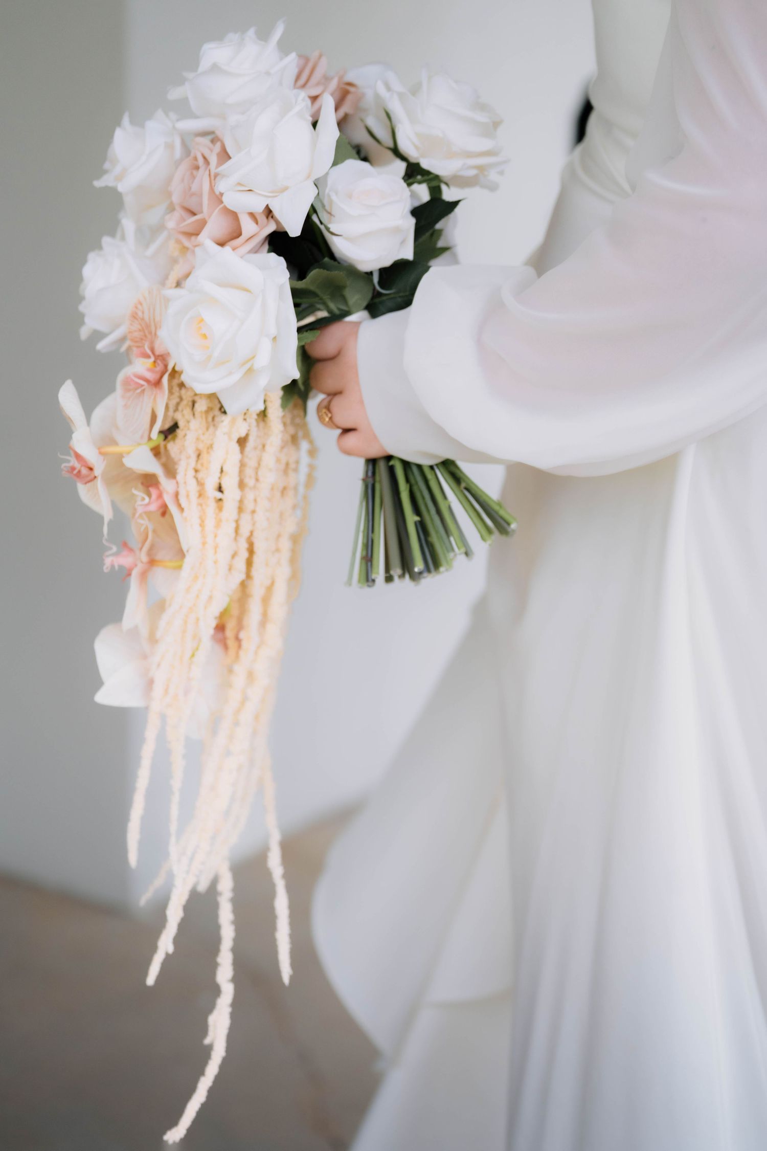 Close-up of bride in white dress holding an elegant bouquet of white and blush roses with trailing amaranthus.