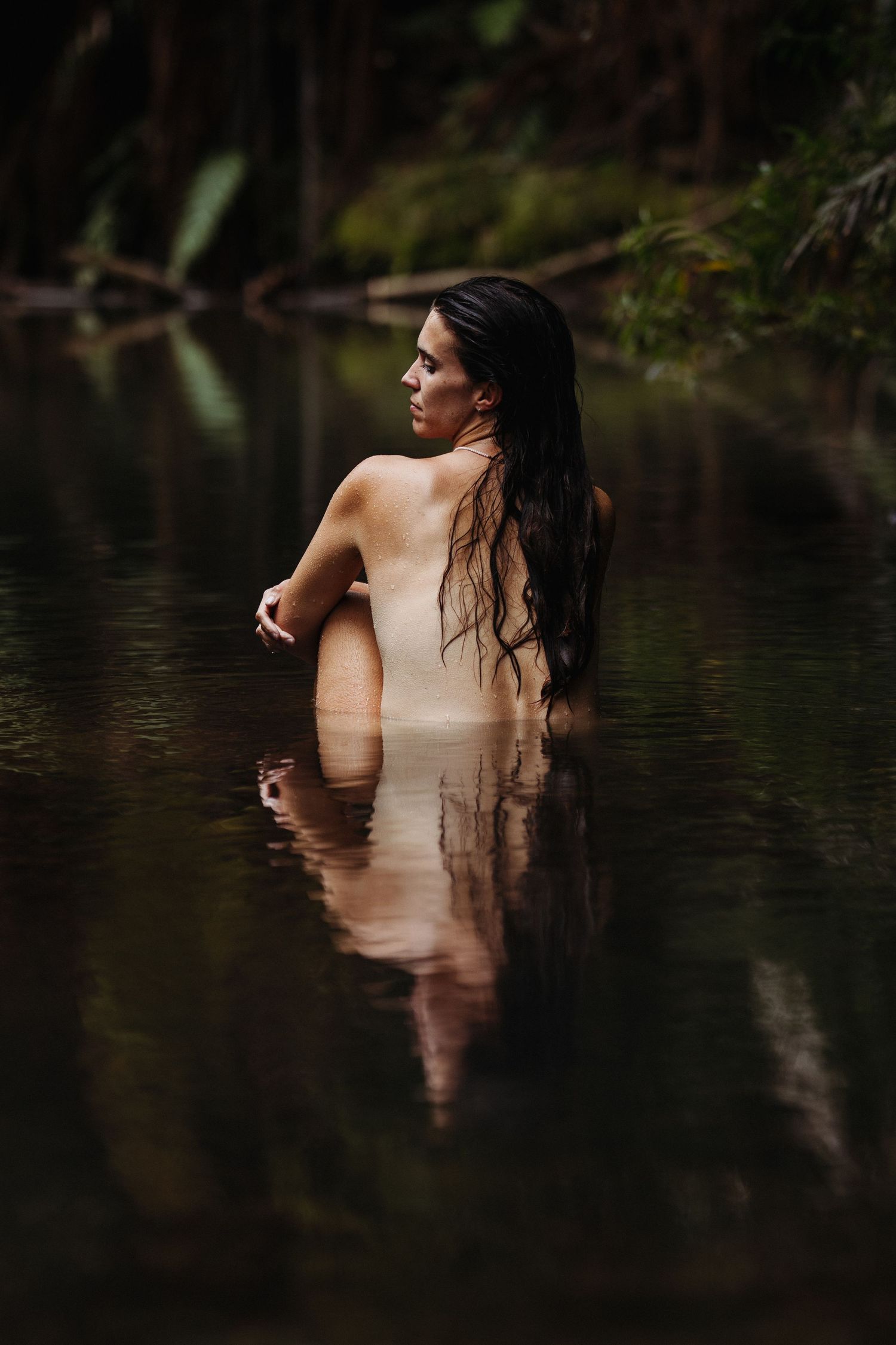 A woman sits in a creek surrounded by native New Zealand bush. Image created by Photography by Chloe