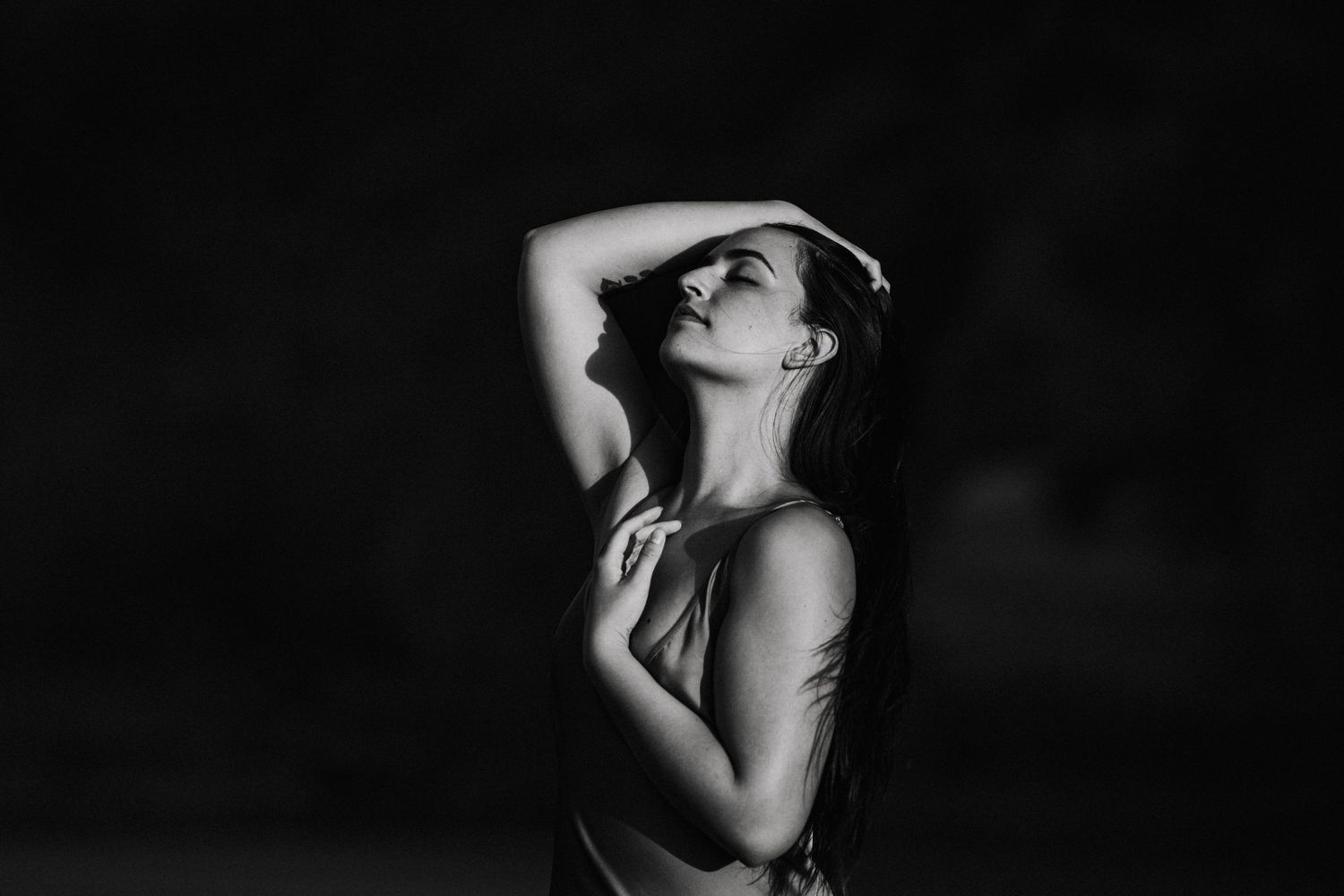 Woman turns her body to the sunshine as she holds her hair and hand to her heart space image created by Waikato portrait photographer
