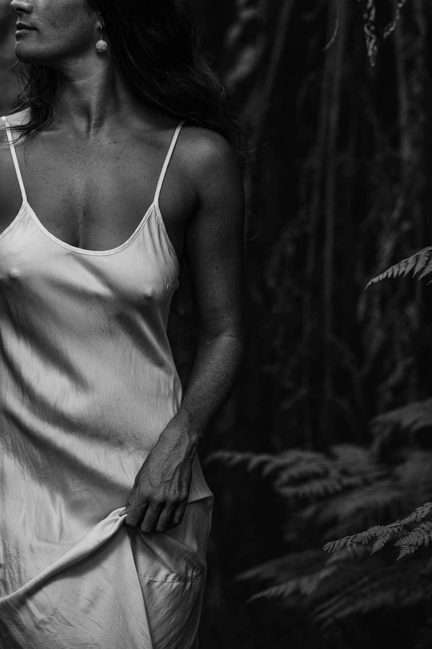 Woman holds her silk dress while looking at ferns in native New Zealand bush, image created by Waikato women portrait photographer
