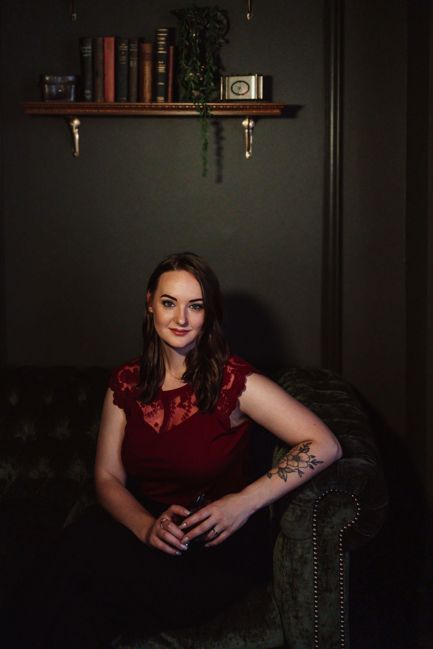 Moody boudoir portrait series in dark setting with burgundy velvet dress against dramatic shadowy background.