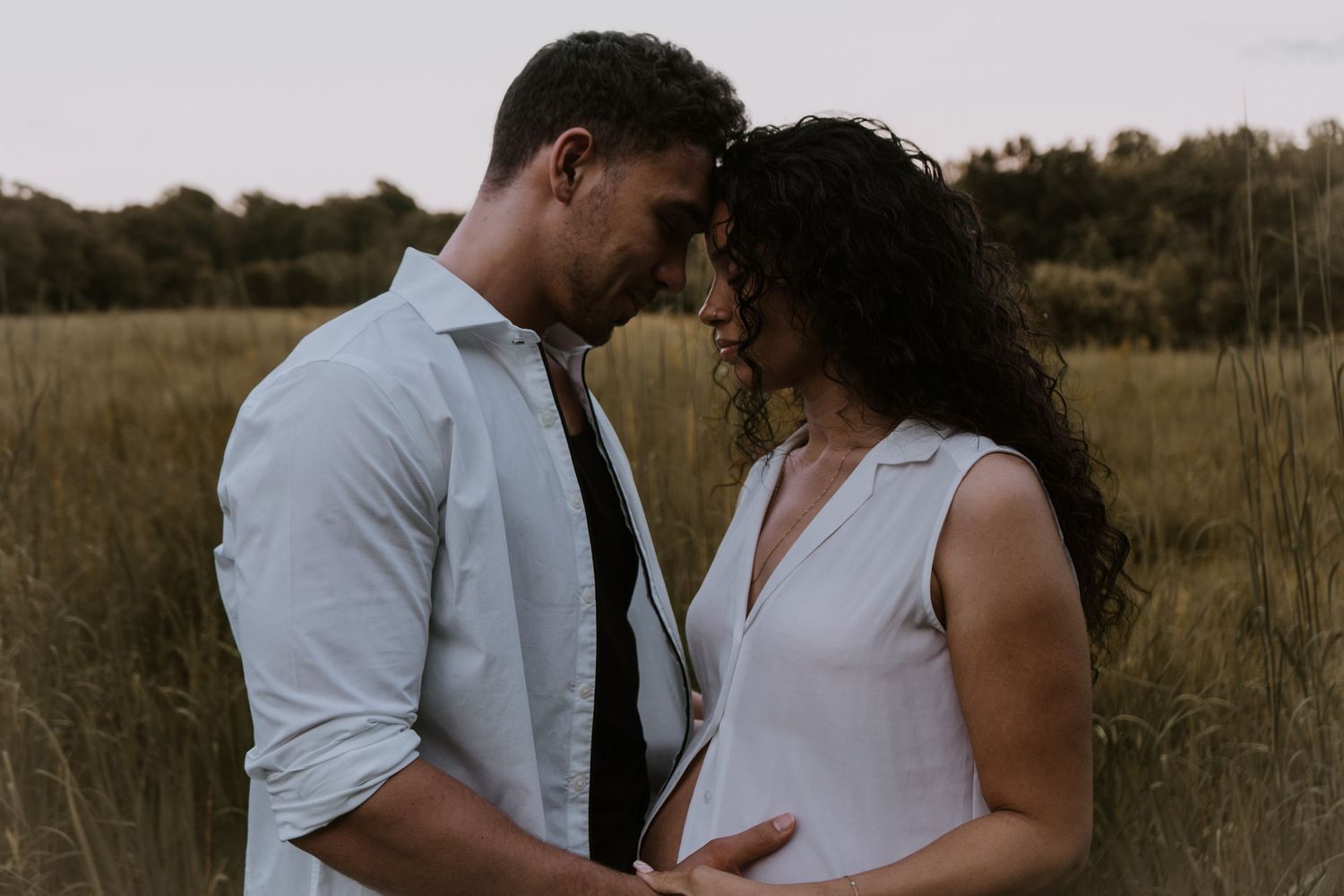 A tender intimate moment between couple in a golden field at sunset, standing close together with romantic energy.