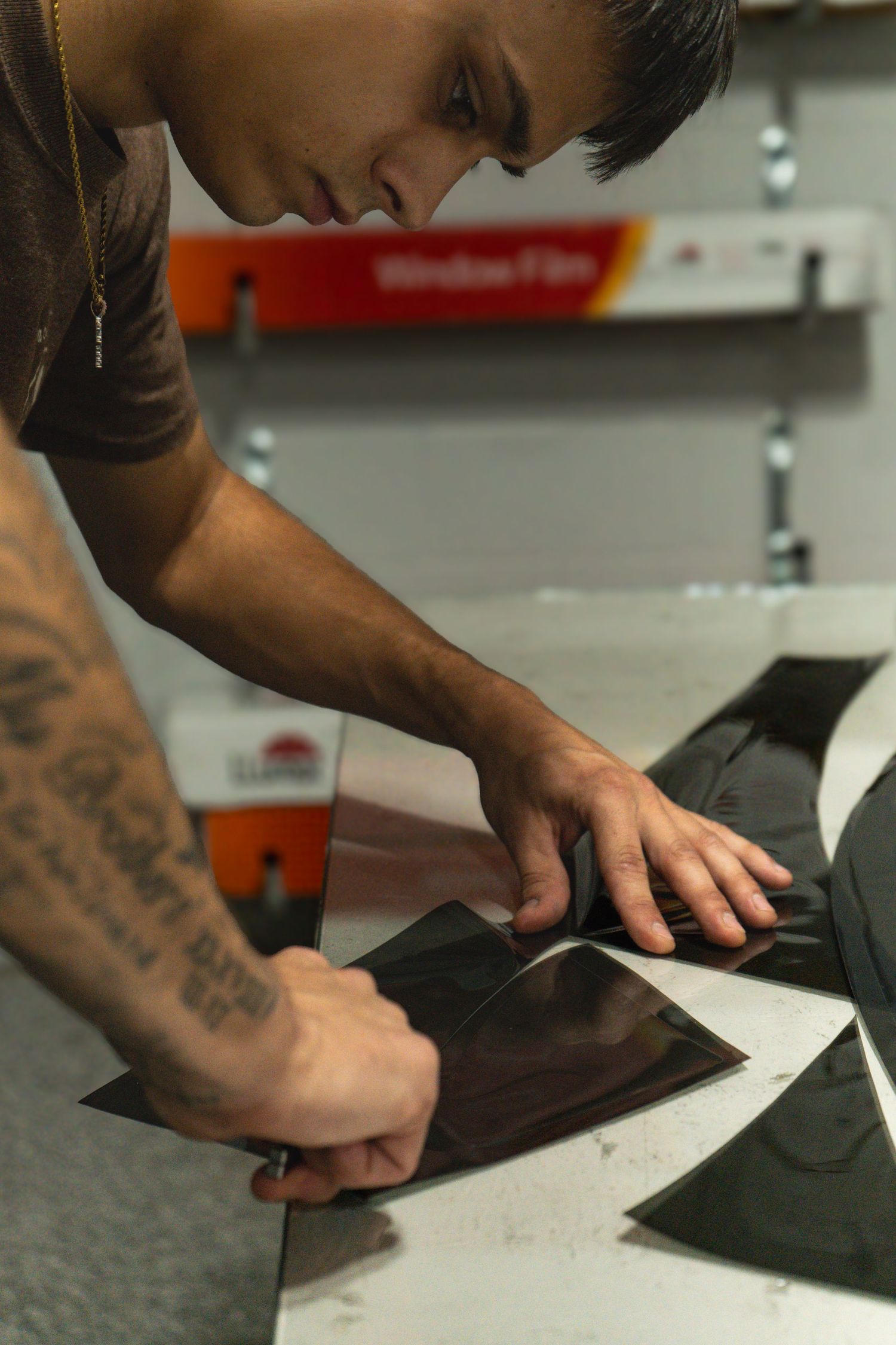 Close-up of tattooed hands measuring and marking dark fabric on a grey surface for sewing or tailoring.