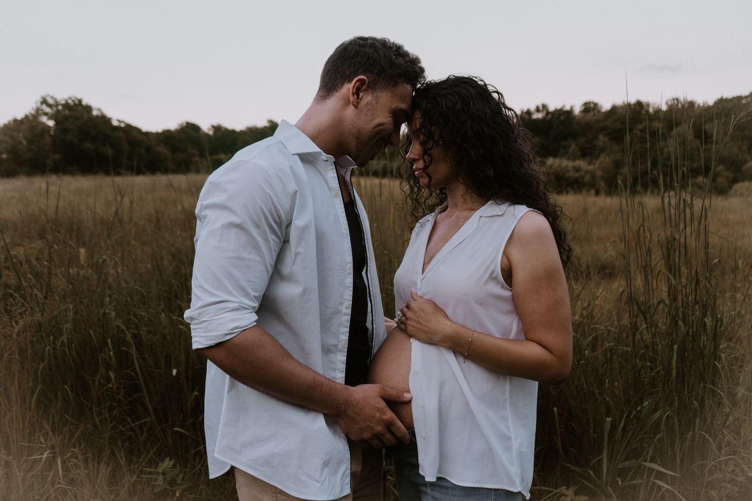 A couple shares an intimate moment together in a golden field at sunset.