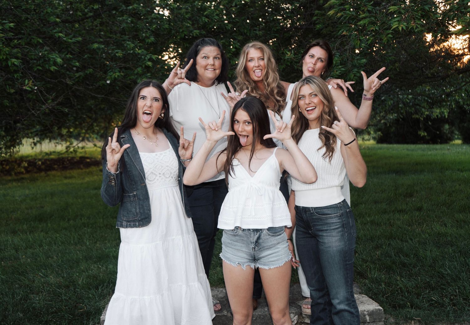A group of friends pose together outdoors wearing casual white tops and jeans.