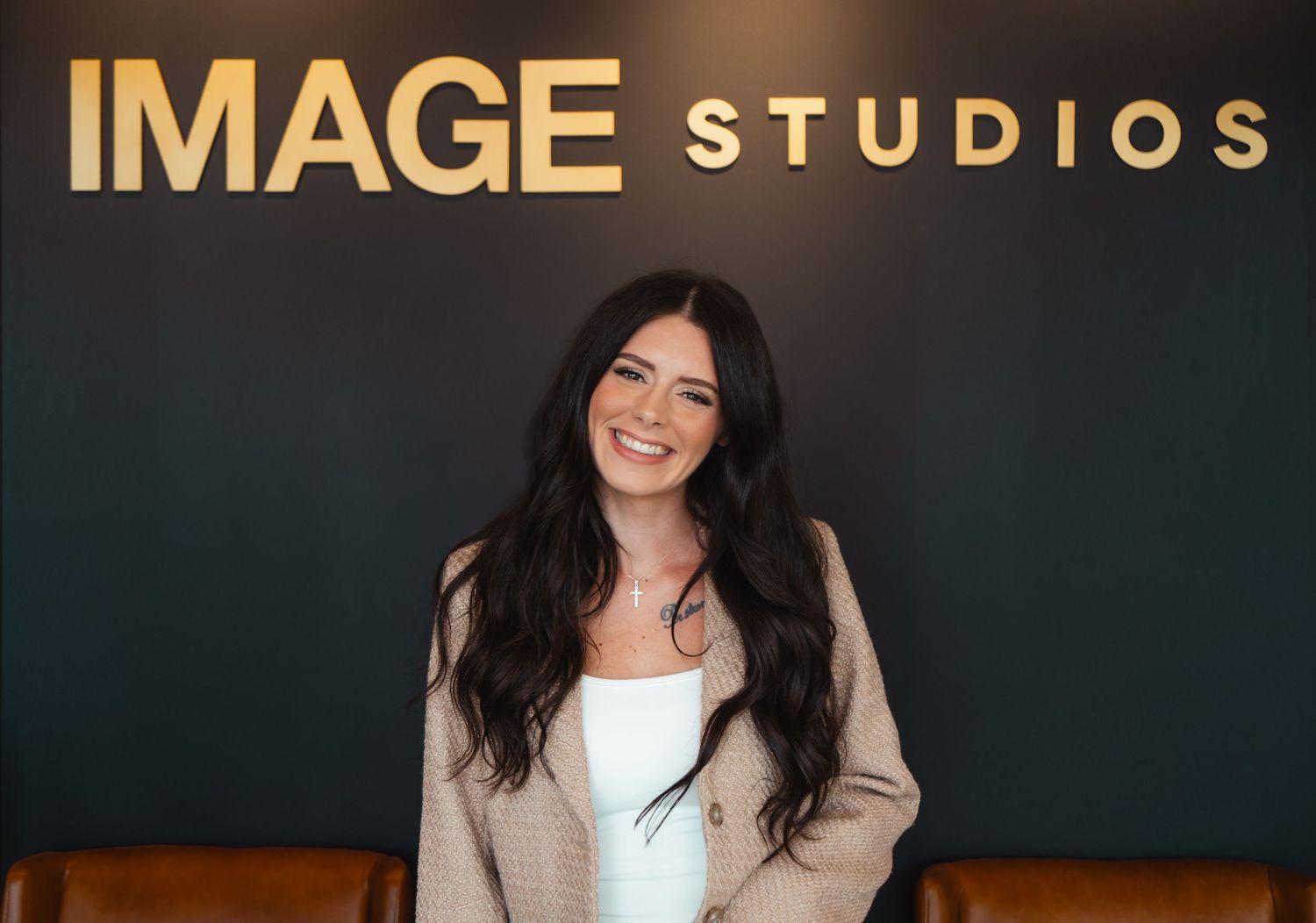 Smiling woman with long dark hair wearing a beige cardigan poses in front of an 'Image Studios' wall sign.