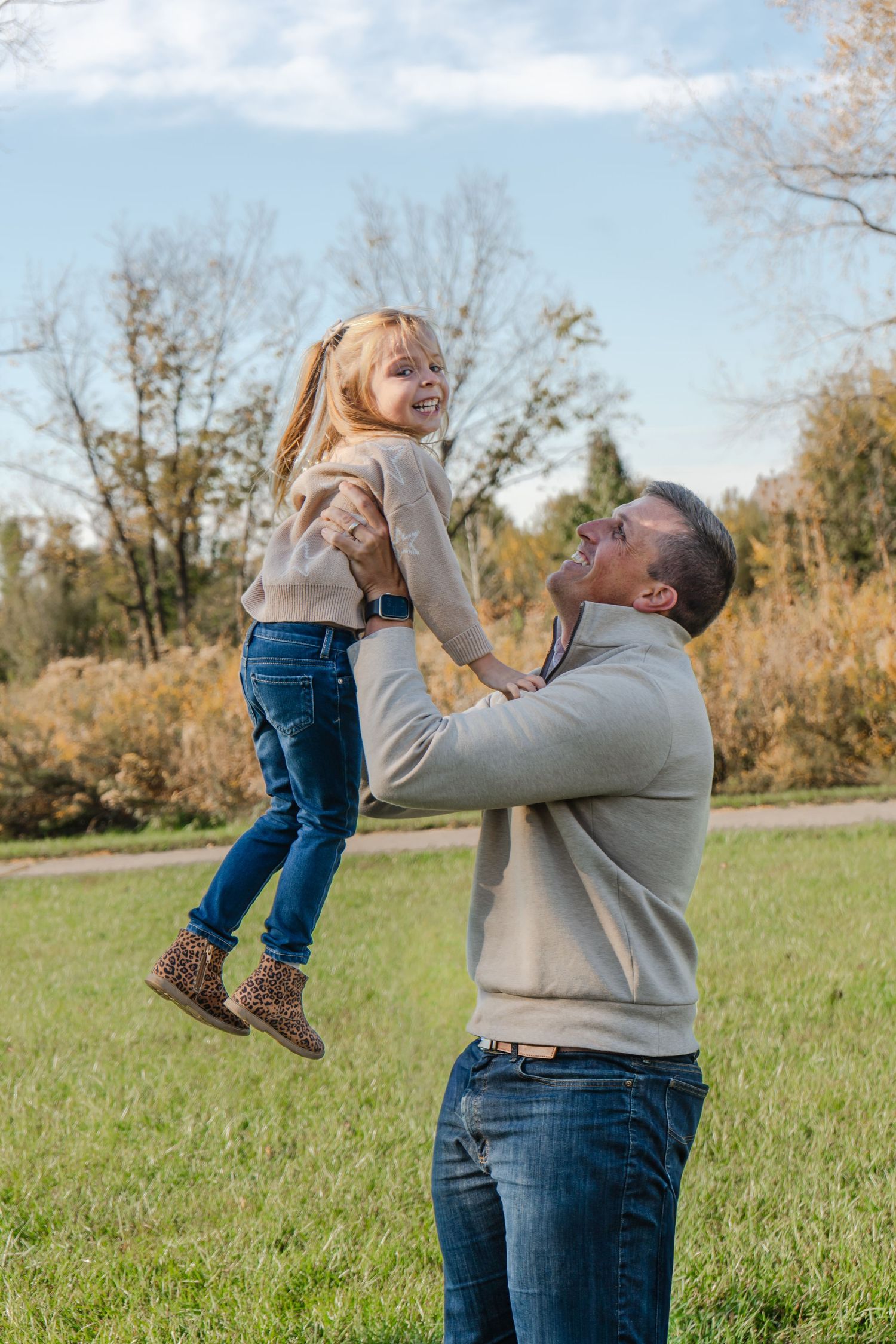 A playful sequence of lifting and spinning a small child in blue jeans on a grassy field during autumn.