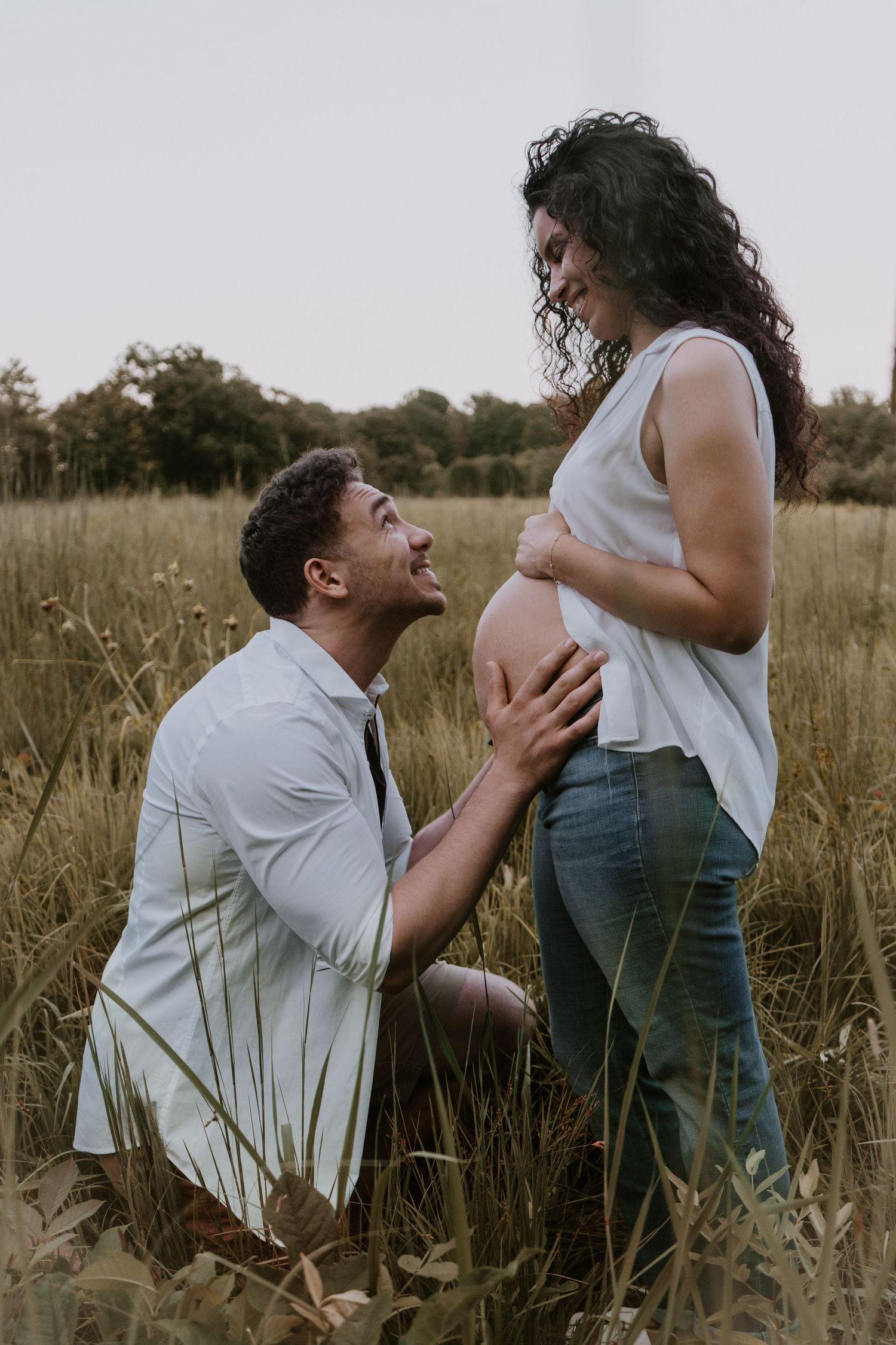 An expecting couple shares an intimate moment in a golden field at sunset as they anticipate their new arrival.