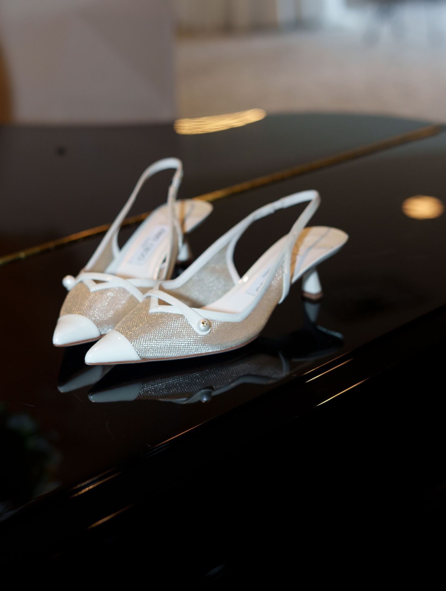 Elegant white slingback kitten heels with glitter mesh detail displayed on a black piano surface.
