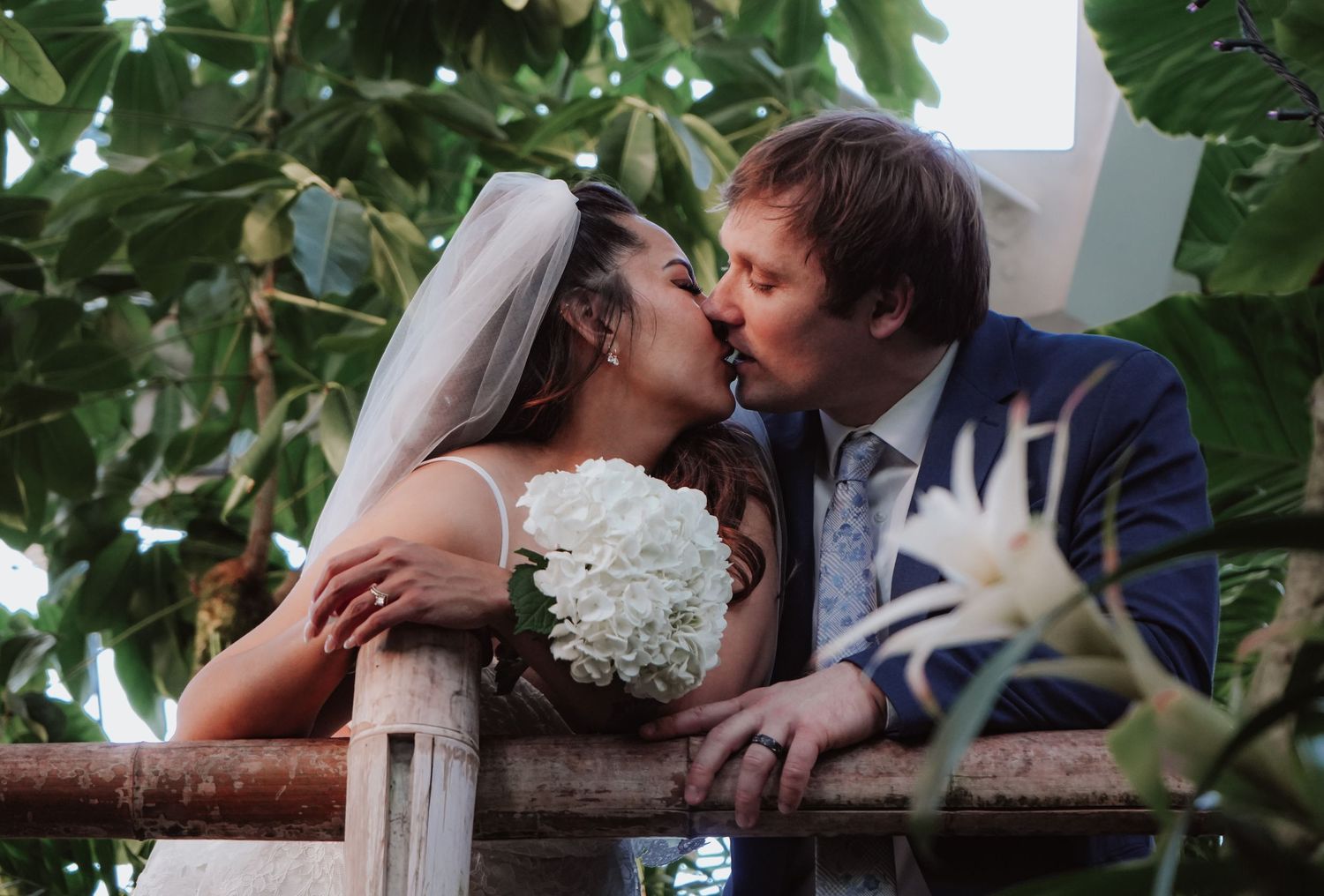 Newlyweds share romantic kiss by foliage during outdoor wedding.