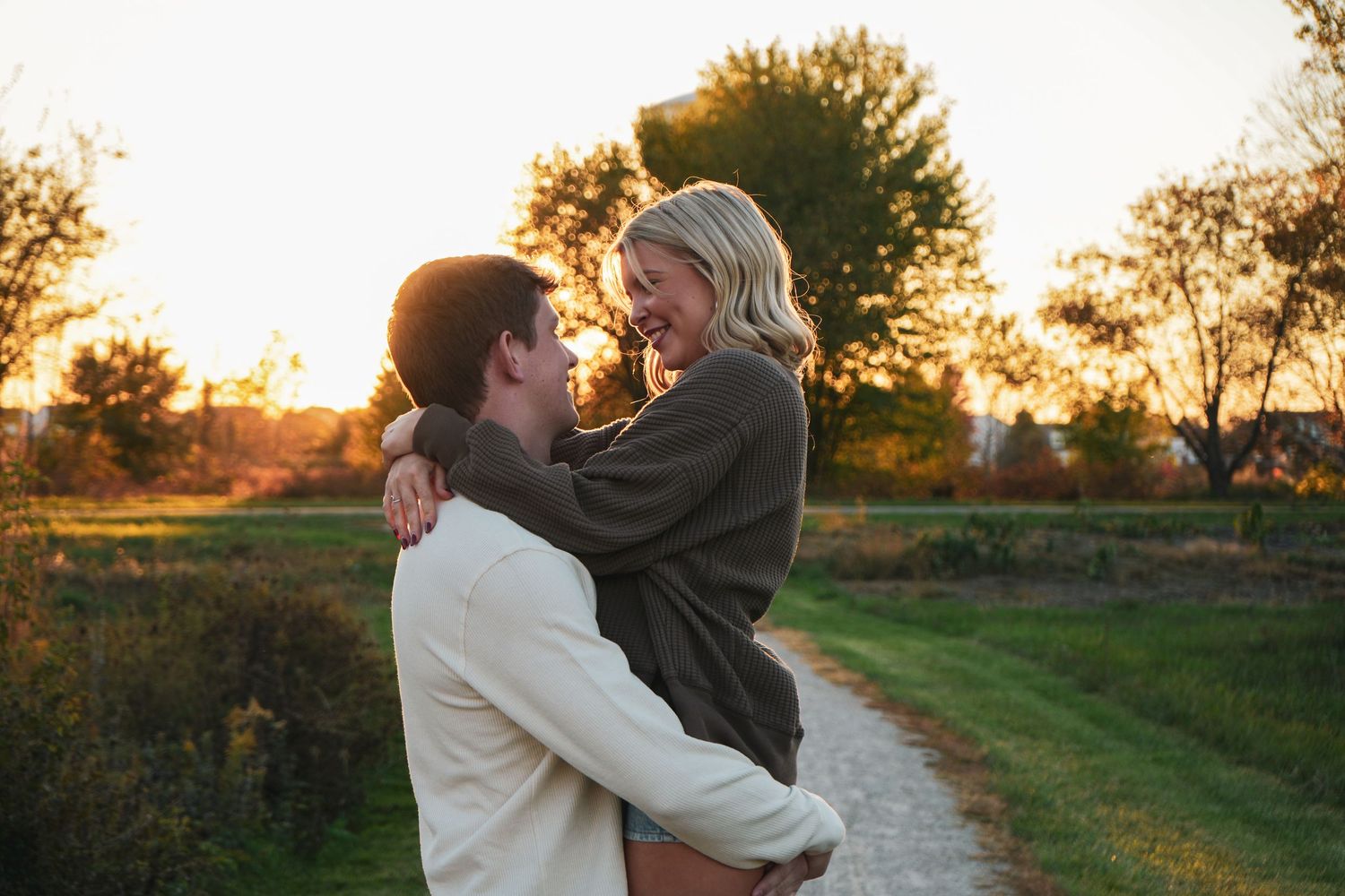 Couple embracing outdoors at sunset on rural path in golden light.