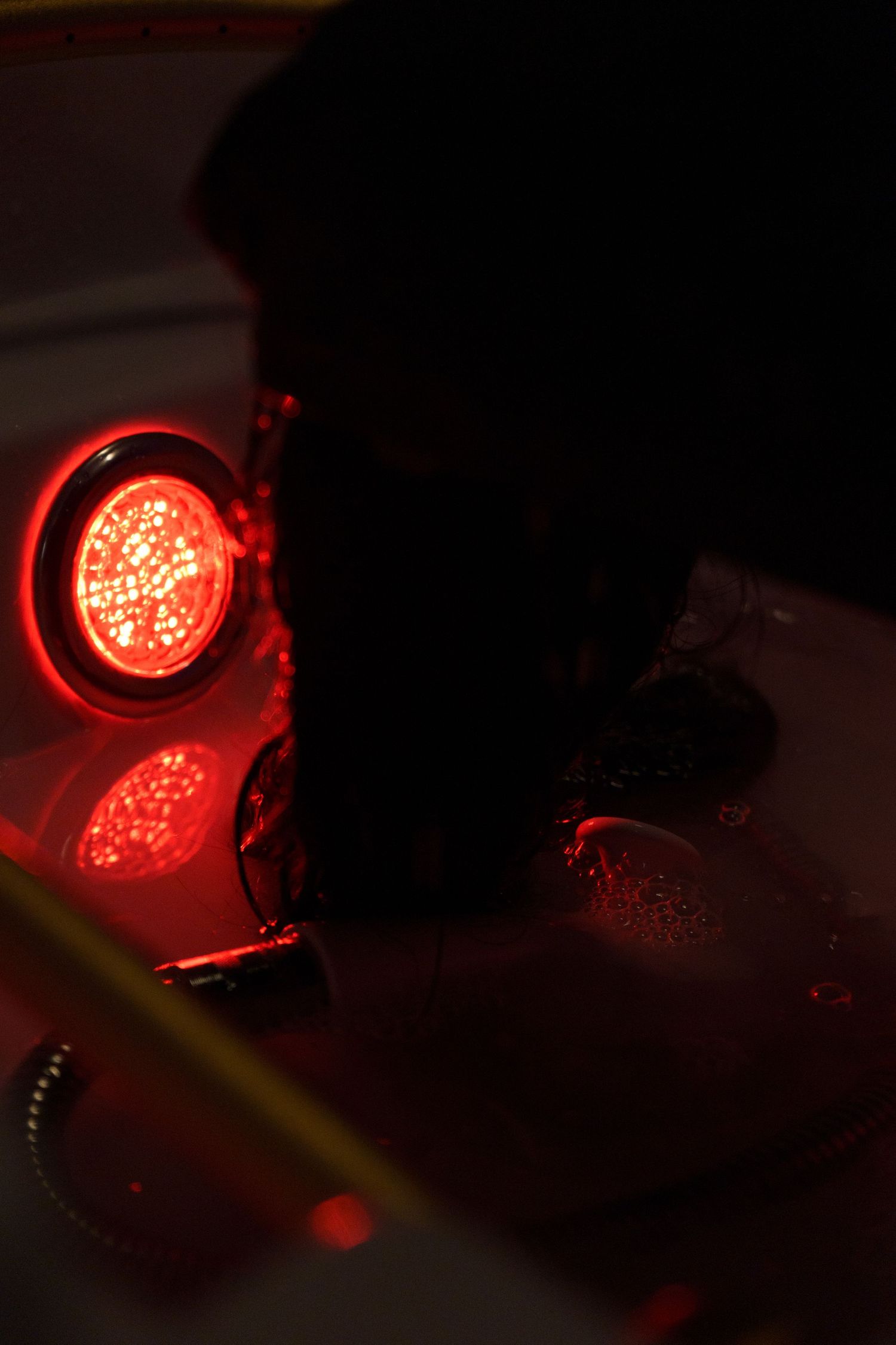 A glowing red LED light illuminates the darkness with its circular pattern and reflection on a shiny surface.
