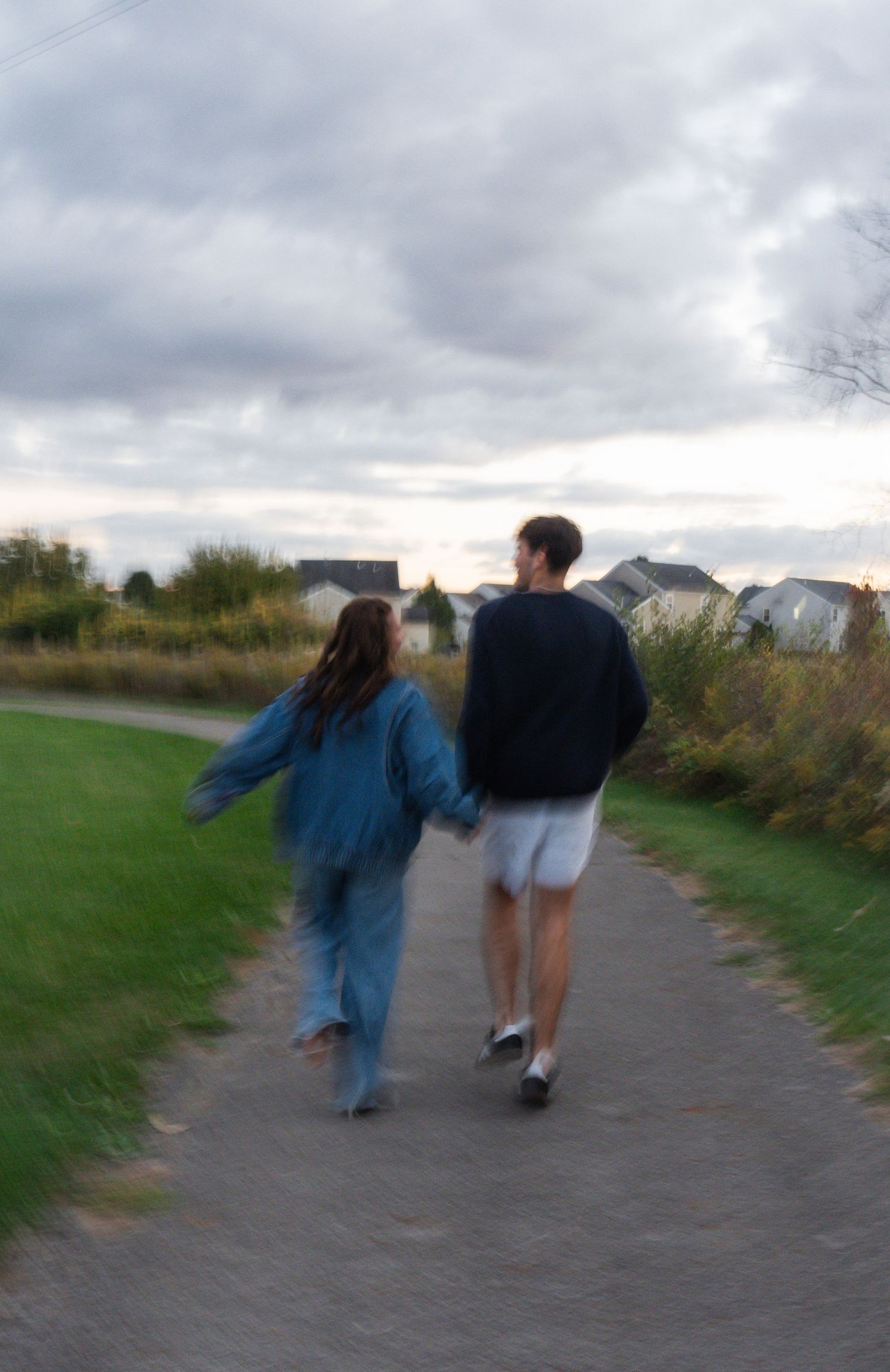 Two people walking together on a path through a grassy area on a cloudy evening.