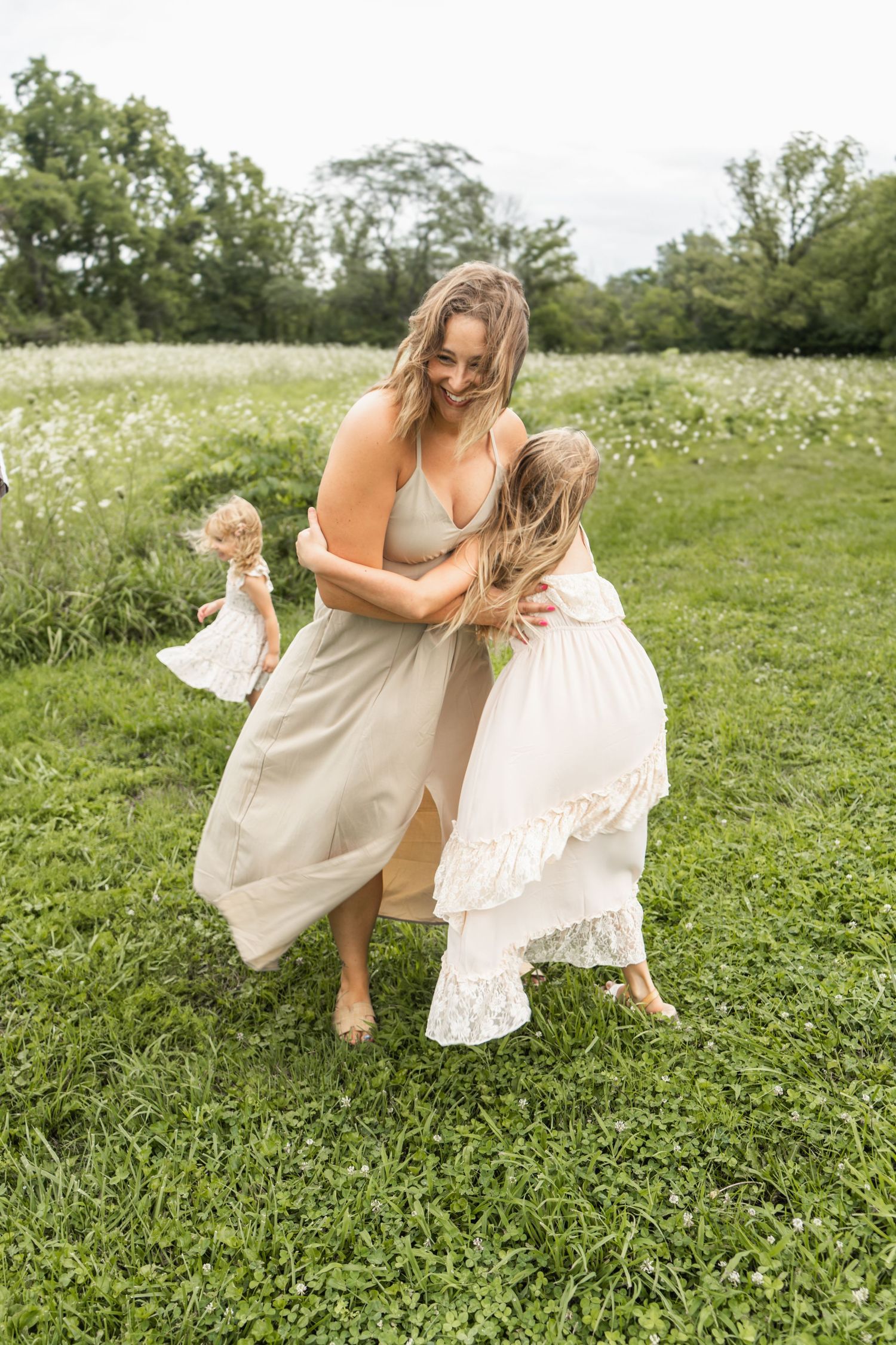 A dancer in a flowing cream dress twirls gracefully through a field of wildflowers and green grass on a sunny day.